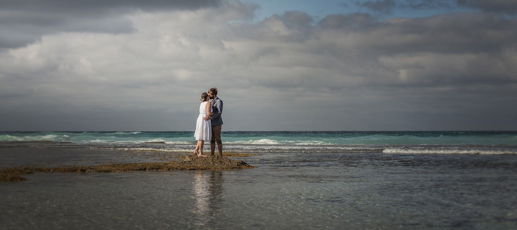 kangaroo island elopement - claire & jacob 35 Claire and Jacob embracing barefoot in shallow water beneath a dramatic cloudy sky on Kangaroo Island