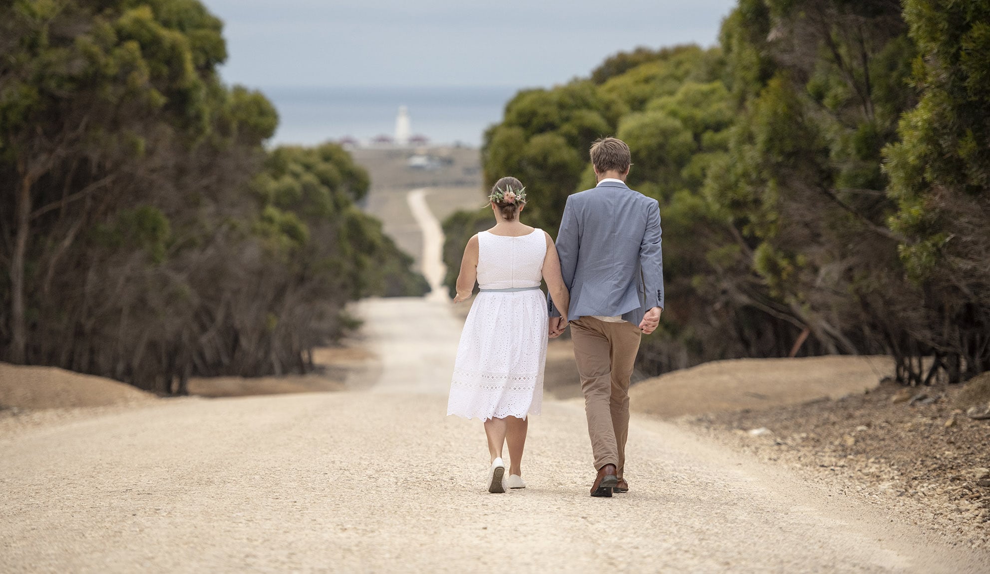 kangaroo island elopement - claire & jacob 16 Eloping couple holding hands as they walk down a tree-lined gravel road towards Cape Willoughby Lighthouse