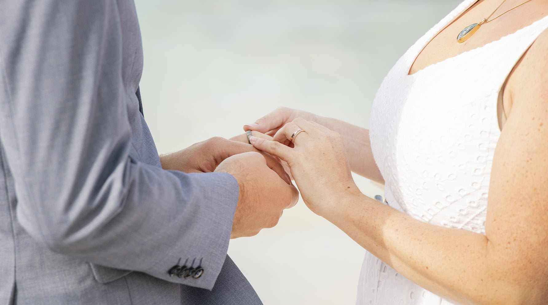kangaroo island elopement - claire & jacob 31 Close-up of a couple exchanging wedding bands, with the bride in a white dress and the groom in a grey suit