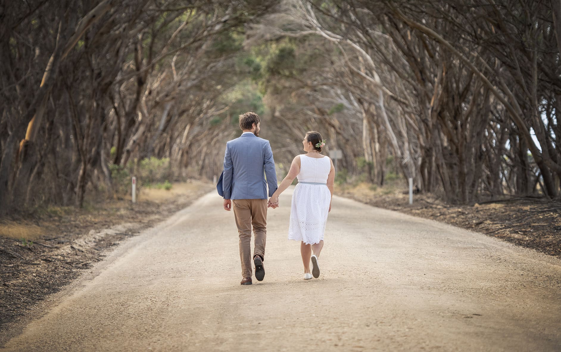 kangaroo island elopement - claire & jacob 13 Claire and Jacob walking hand in hand along a tree-lined dirt road on Kangaroo Island