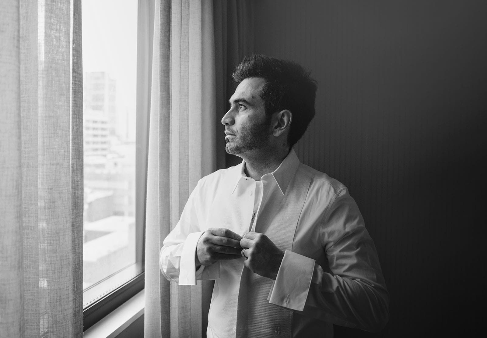 adelaide bridal photoshoot and reception - emre & sara 6 Groom buttoning shirt looking out window