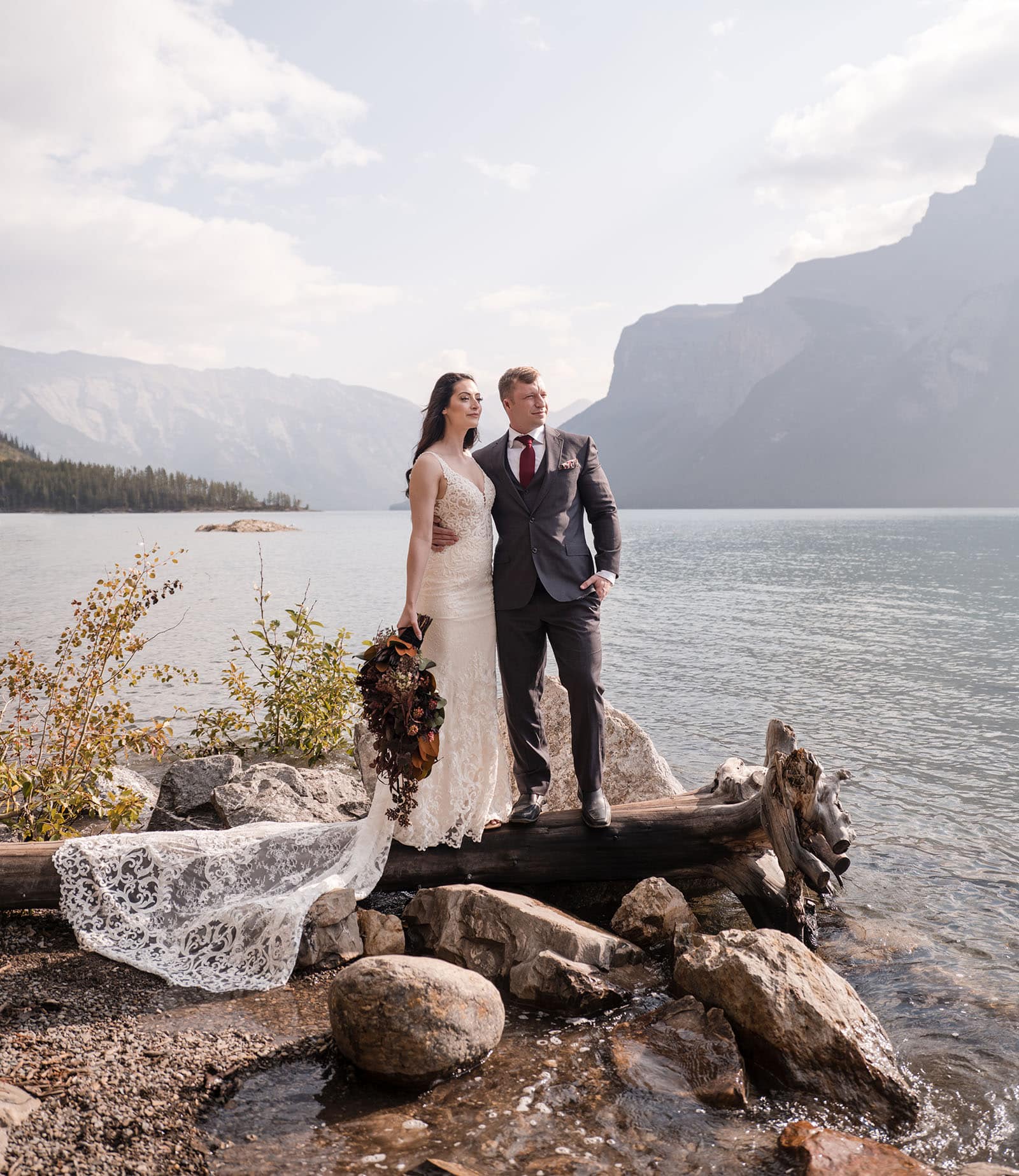 canada's lake louise wedding photoshoot - melodie & brandon 9 Bridal couple standing on the shore of Lake Minnewanka
