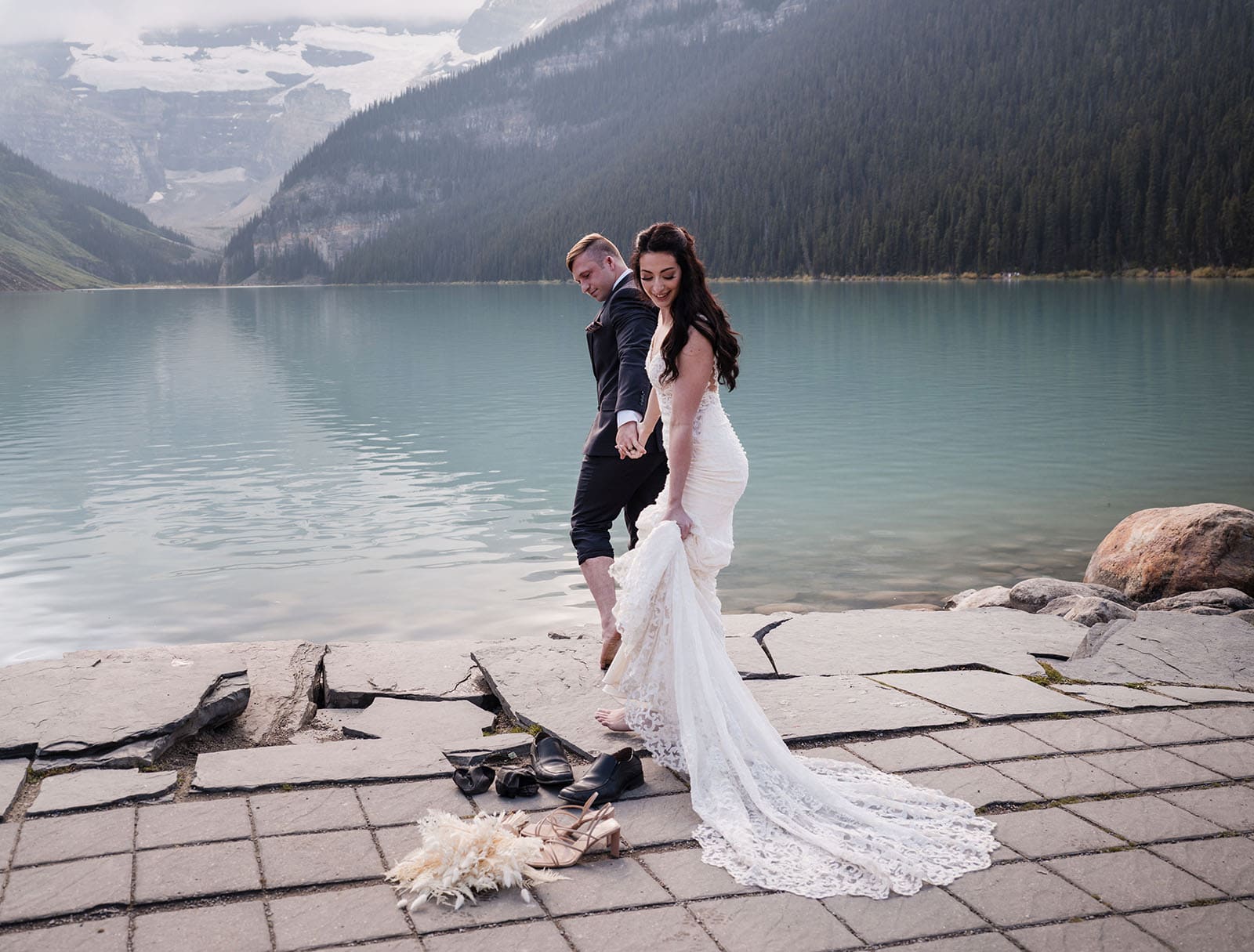 canada's lake louise wedding photoshoot - melodie & brandon 15 Bride and groom taking off shoes to get into lake