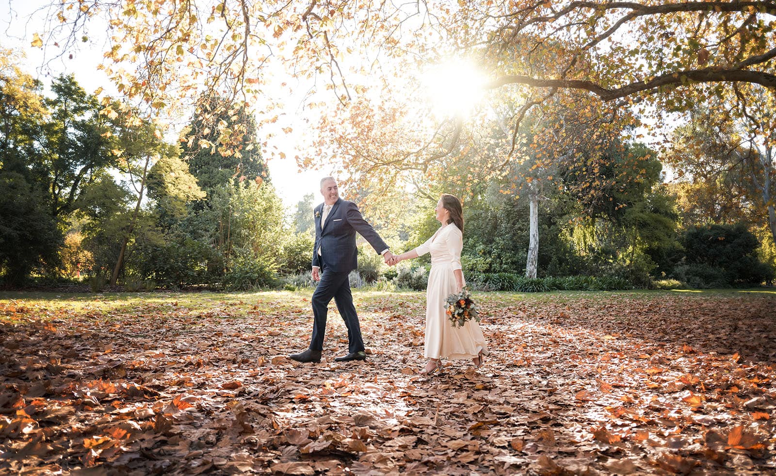 northern palm garden wedding - nicole & daryl 134 groom leading bride through autumn leaves
