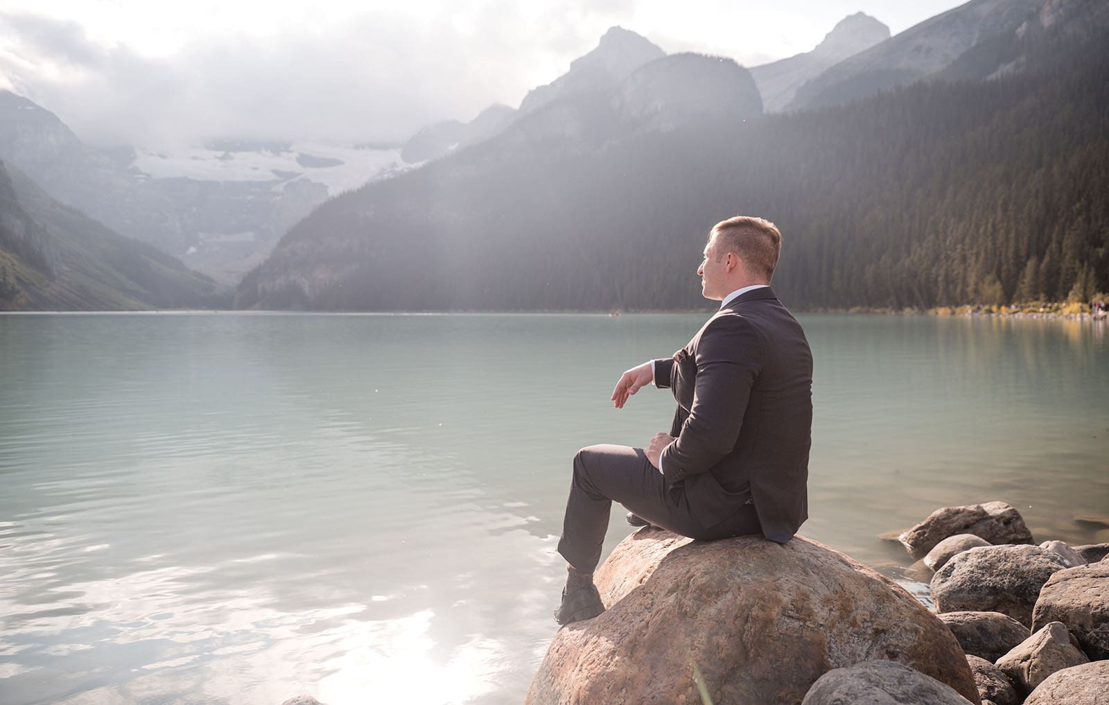 canada's lake louise wedding photoshoot - melodie & brandon 21 Groom sitting on shore of Lake Louise