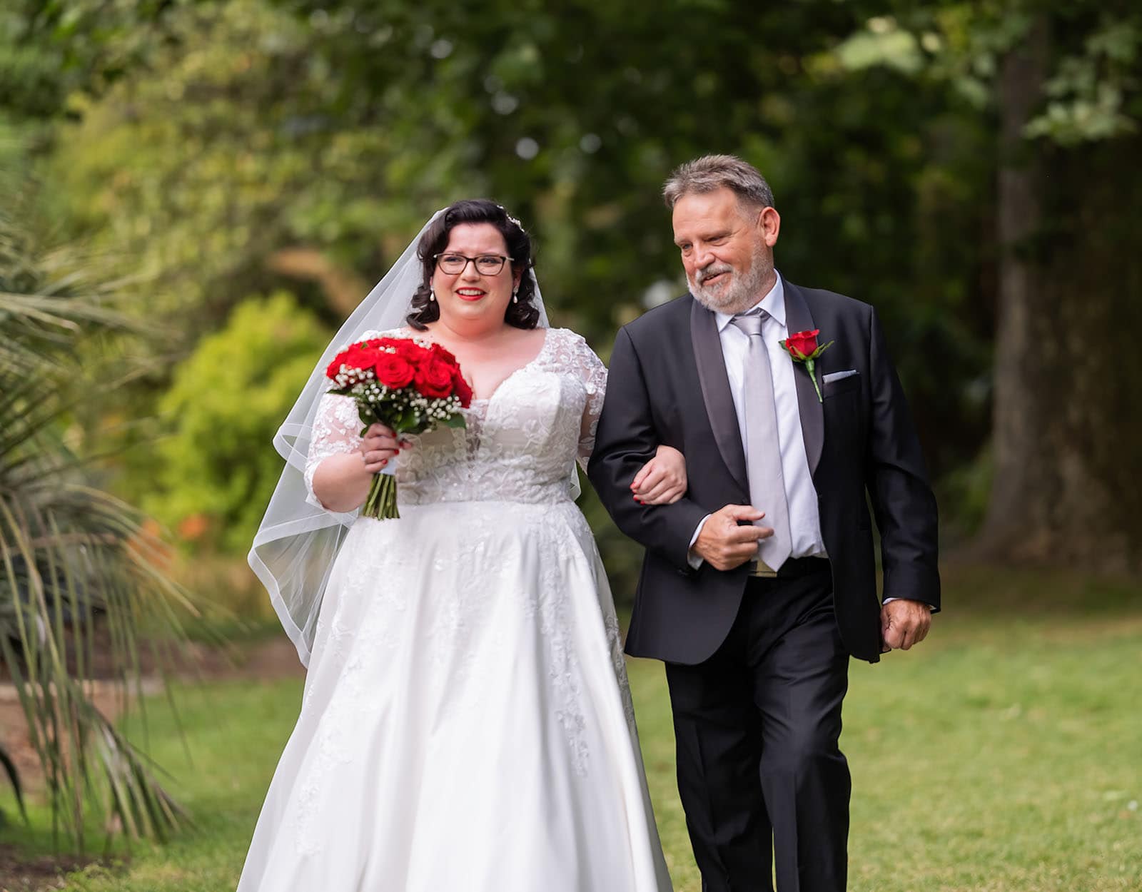 botanic gardens palm house wedding - kelly & david 92 Bride in a lace wedding gown holding red roses walks arm in arm with her father through Adelaide Botanic Gardens.