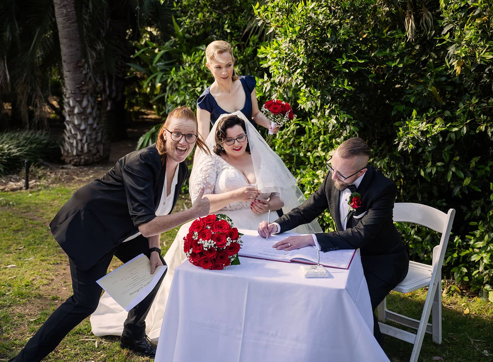 botanic gardens palm house wedding - kelly & david 102 Celebrant leans into frame as the groom signs the wedding register beside the bride at Adelaide Botanic Gardens.