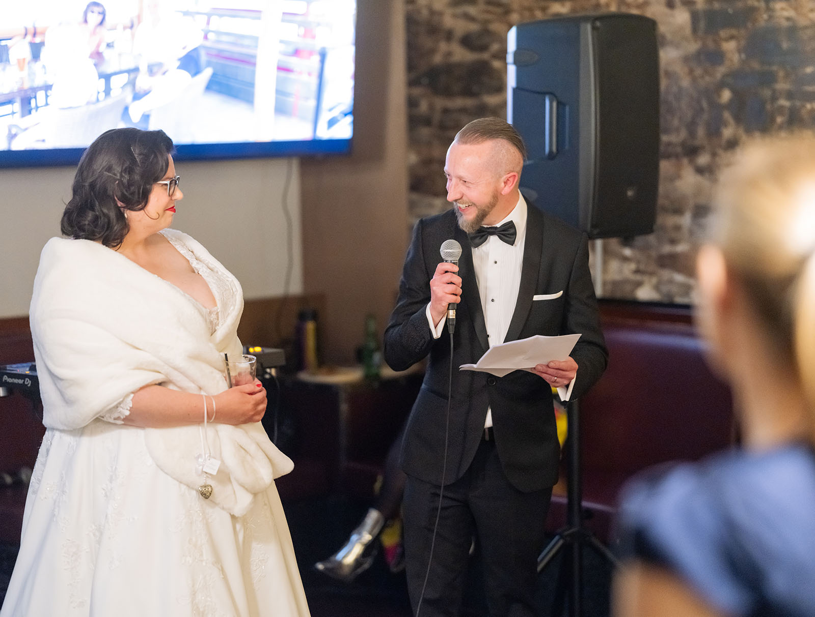 botanic gardens palm house wedding - kelly & david 133 David in a tuxedo giving a wedding speech with a microphone as Kelly smiles beside him