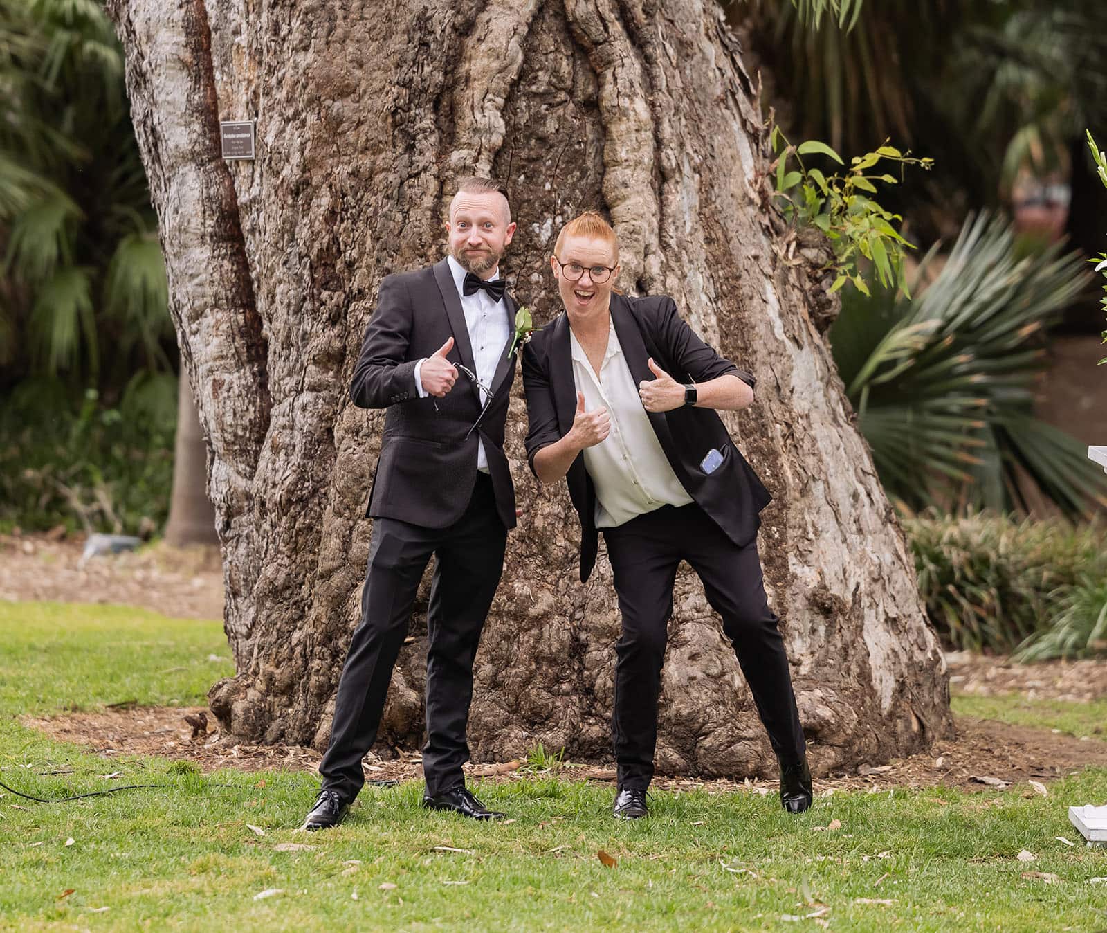 botanic gardens palm house wedding - kelly & david 90 Groom in a black tuxedo and celebrant giving thumbs up beside a large gum tree at Adelaide Botanic Gardens