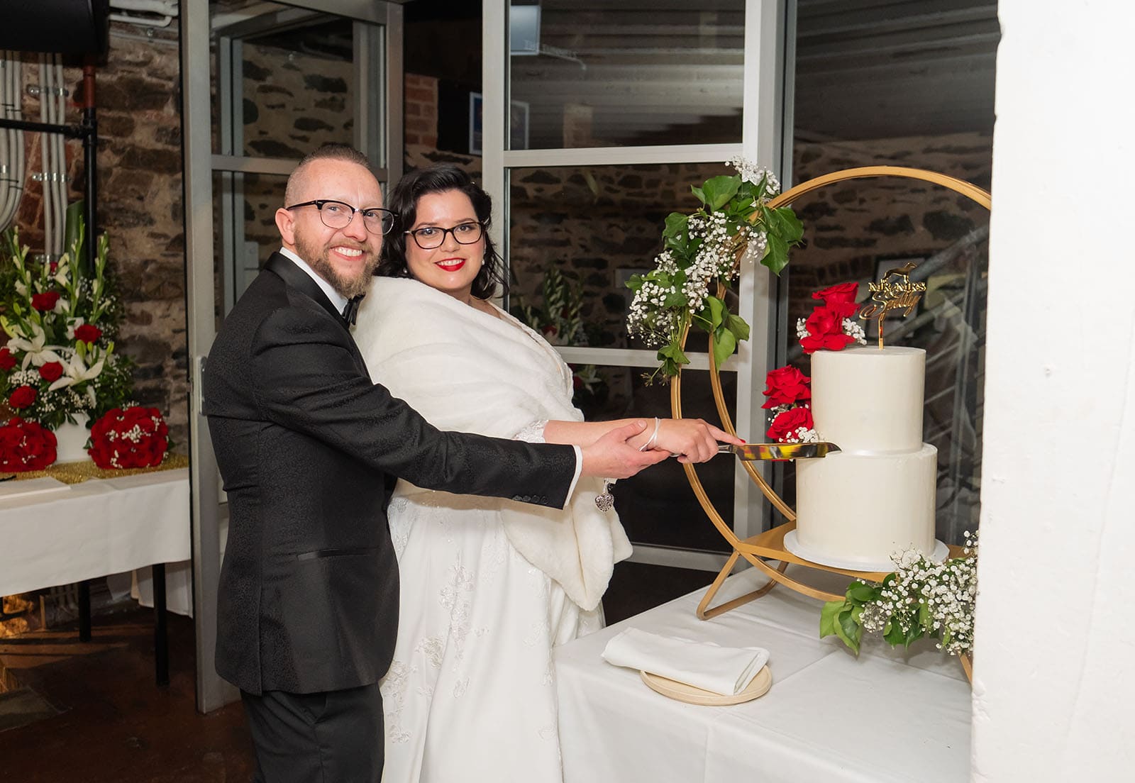 botanic gardens palm house wedding - kelly & david 128 Kelly and David cutting their two-tier wedding cake decorated with red roses and greenery