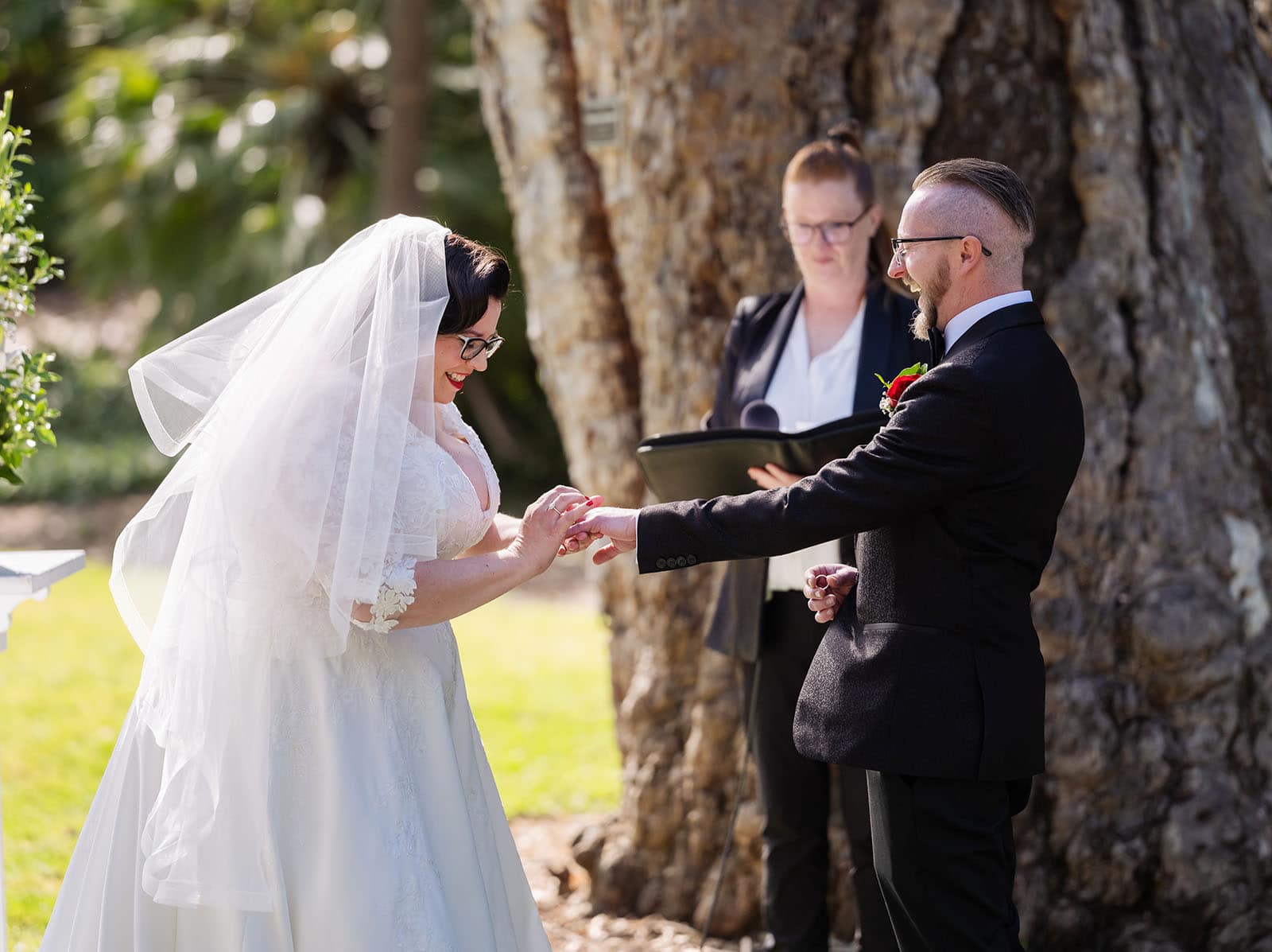 botanic gardens palm house wedding - kelly & david 100 Kelly and David smiling as they exchange rings beneath a large gum tree during their Adelaide Botanic Gardens wedding ceremony