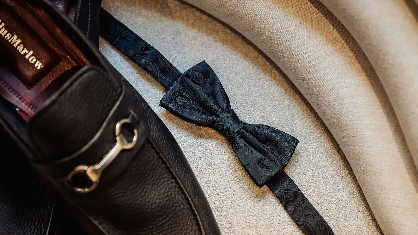 botanic gardens, araucaria avenue wedding - jade & hazim 1 Elegant paisley-patterned black bow tie and high-quality leather bag on contrasting background.