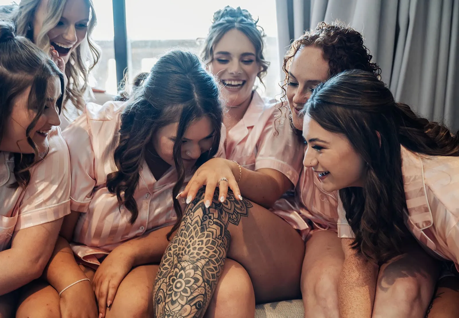 botanic gardens, araucaria avenue wedding - jade & hazim 15 Bride-to-be in pink pyjamas with friends admiring a floral tattoo at indoor celebration.