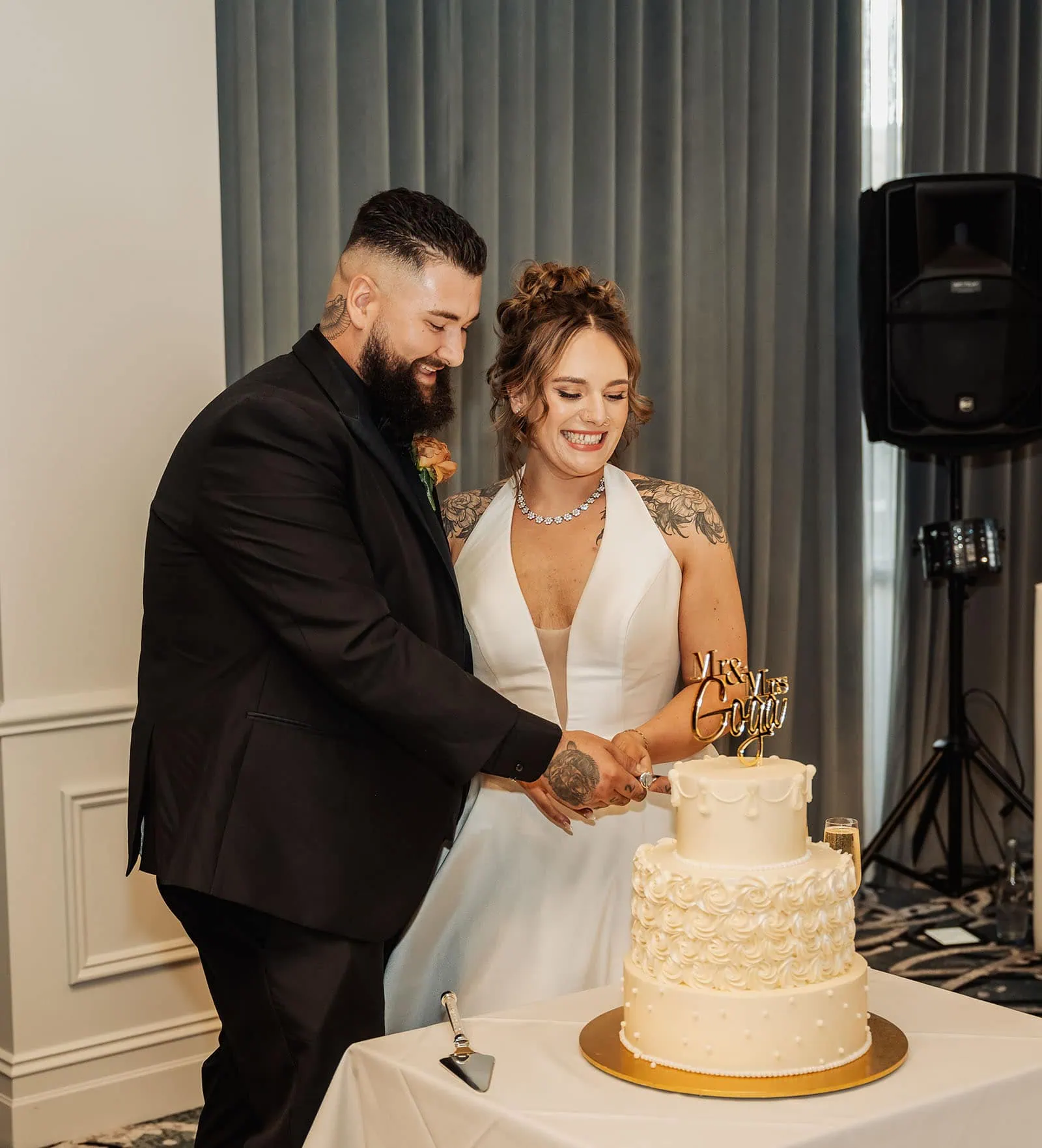 botanic gardens, araucaria avenue wedding - jade & hazim 63 Happily tattooed couple cutting three-tiered wedding cake at indoor celebration.