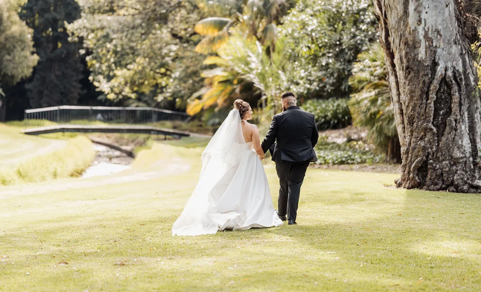 botanic gardens, araucaria avenue wedding - jade & hazim 45 Bride and groom holding hands while walking in lush garden after wedding ceremony.