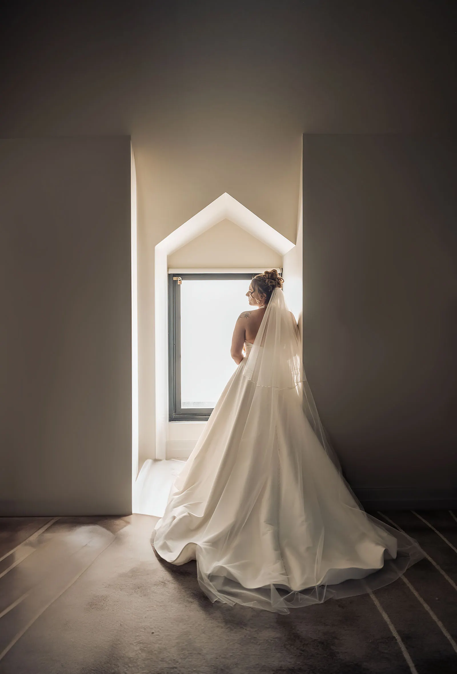 botanic gardens, araucaria avenue wedding - jade & hazim 22 Bride in white gown standing by an A-frame window before wedding ceremony.