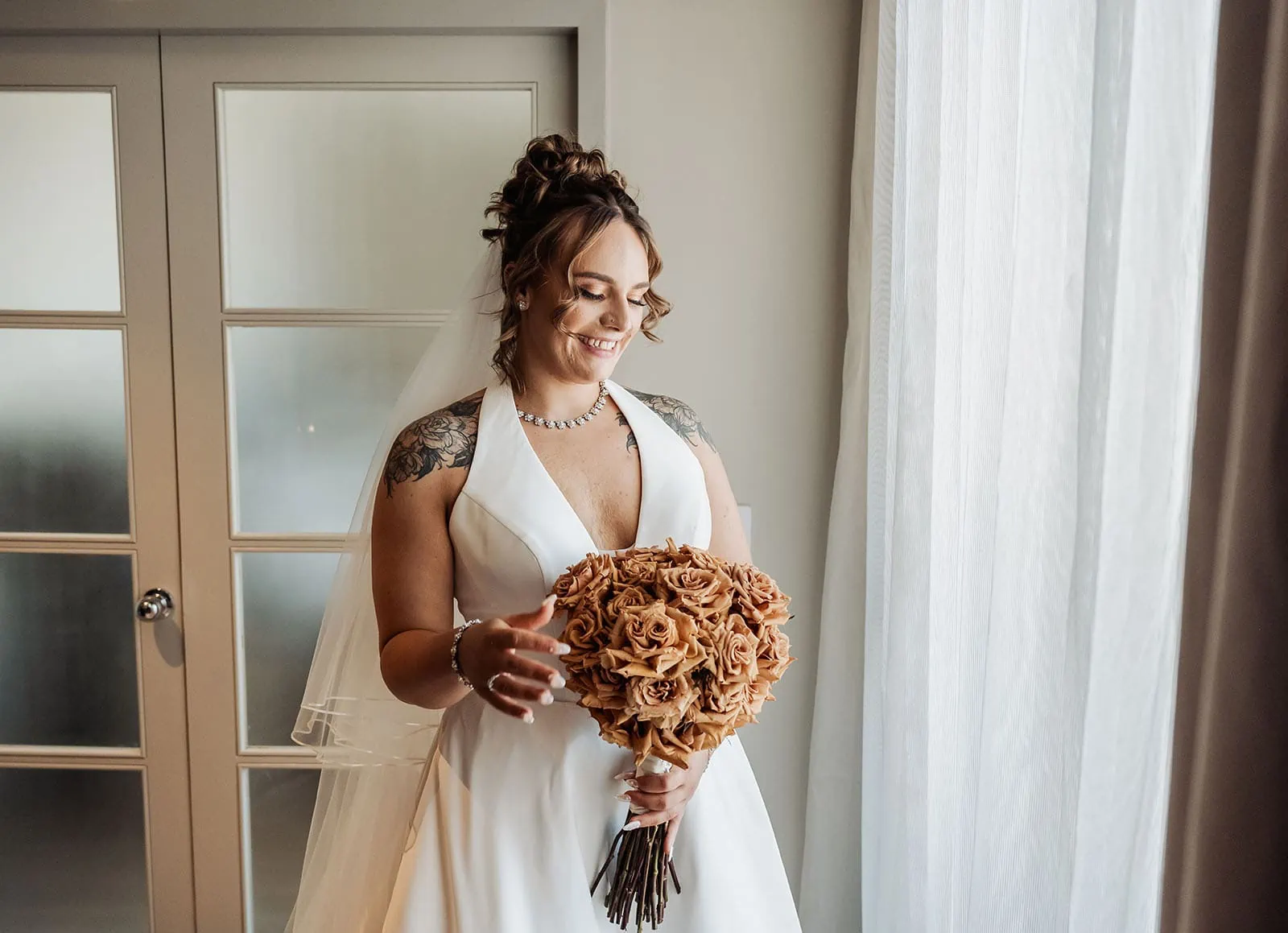 botanic gardens, araucaria avenue wedding - jade & hazim 25 Bride with tattoos smiling, holding an earth-toned rose bouquet in a white wedding gown.