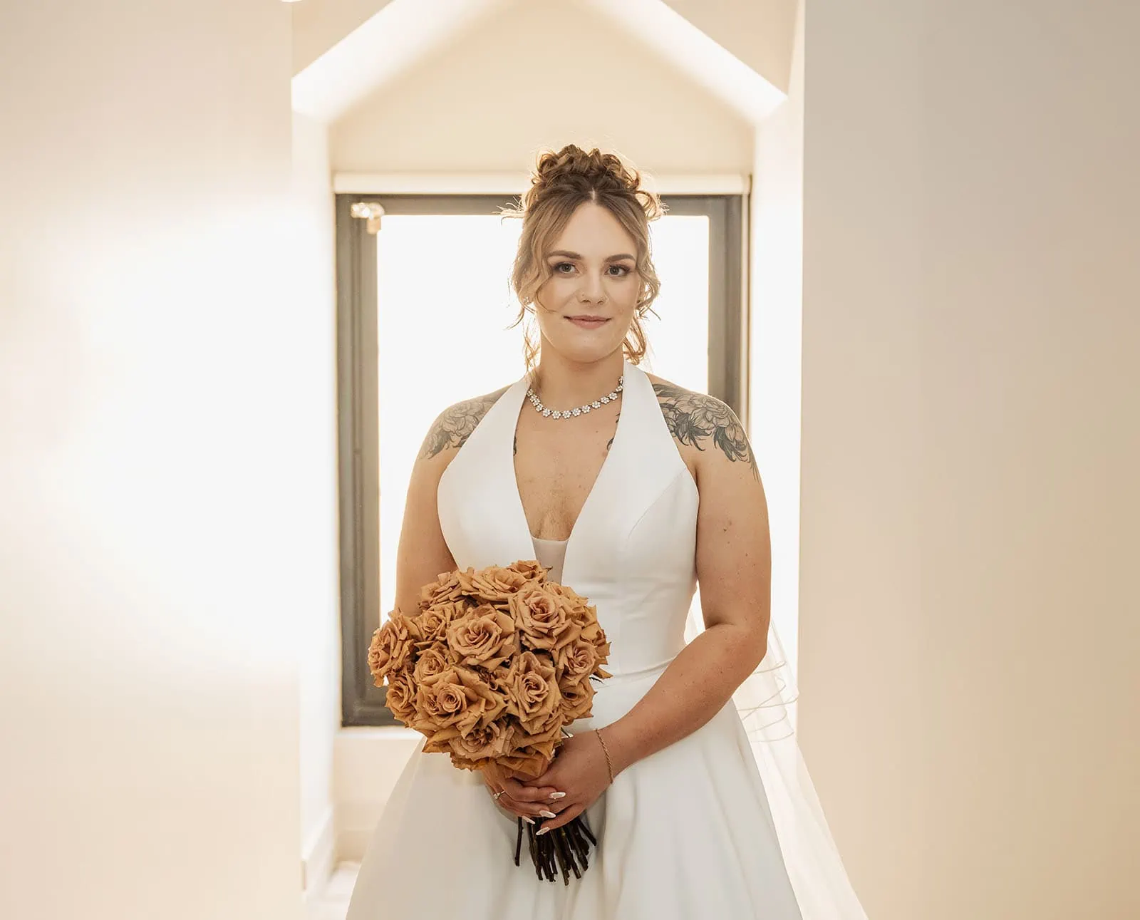 botanic gardens, araucaria avenue wedding - jade & hazim 23 Elegant bride in white wedding gown holding a rose bouquet in a modern room.