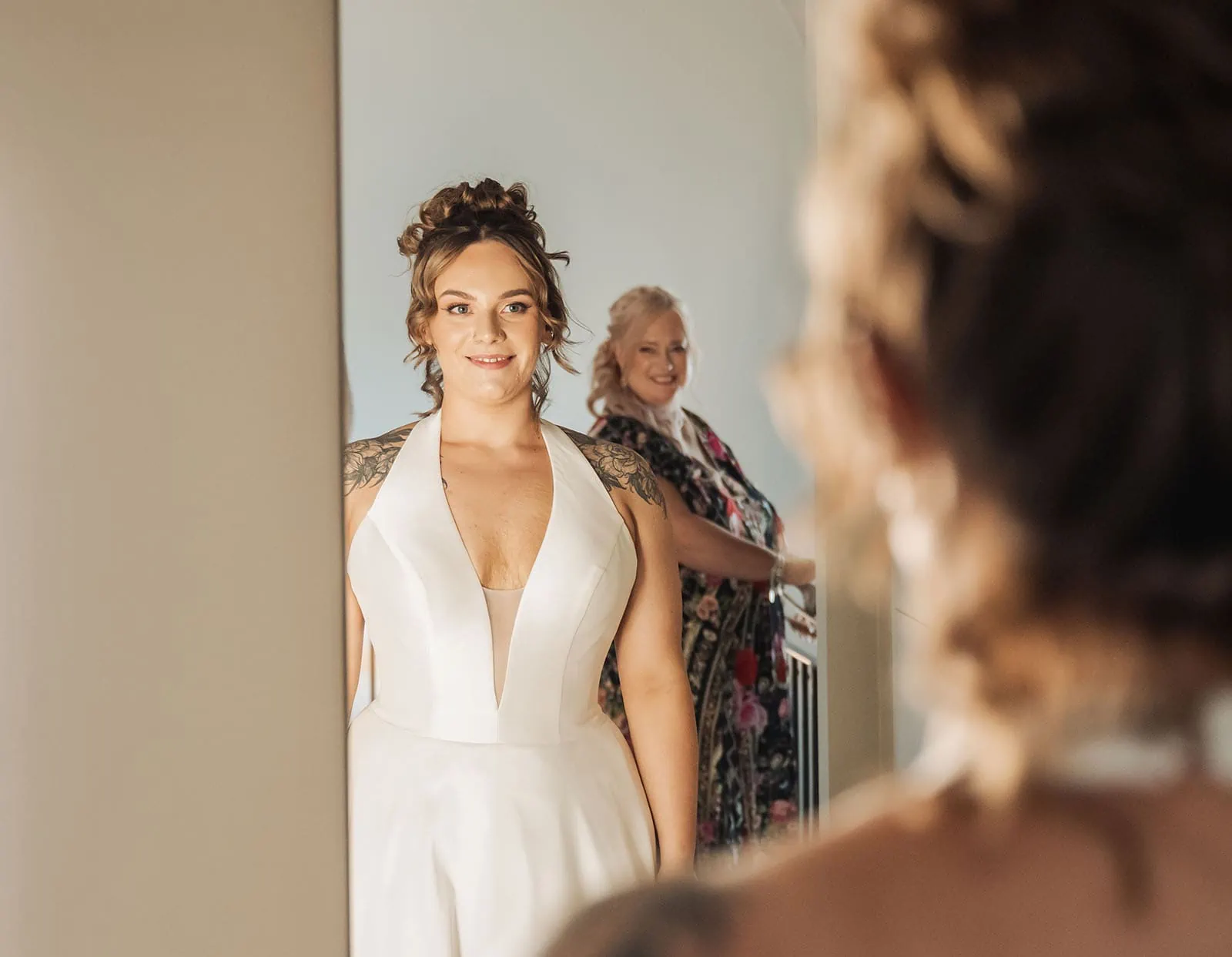 botanic gardens, araucaria avenue wedding - jade & hazim 19 Bride in white dress admiring her reflection before wedding, with a friend looking on.