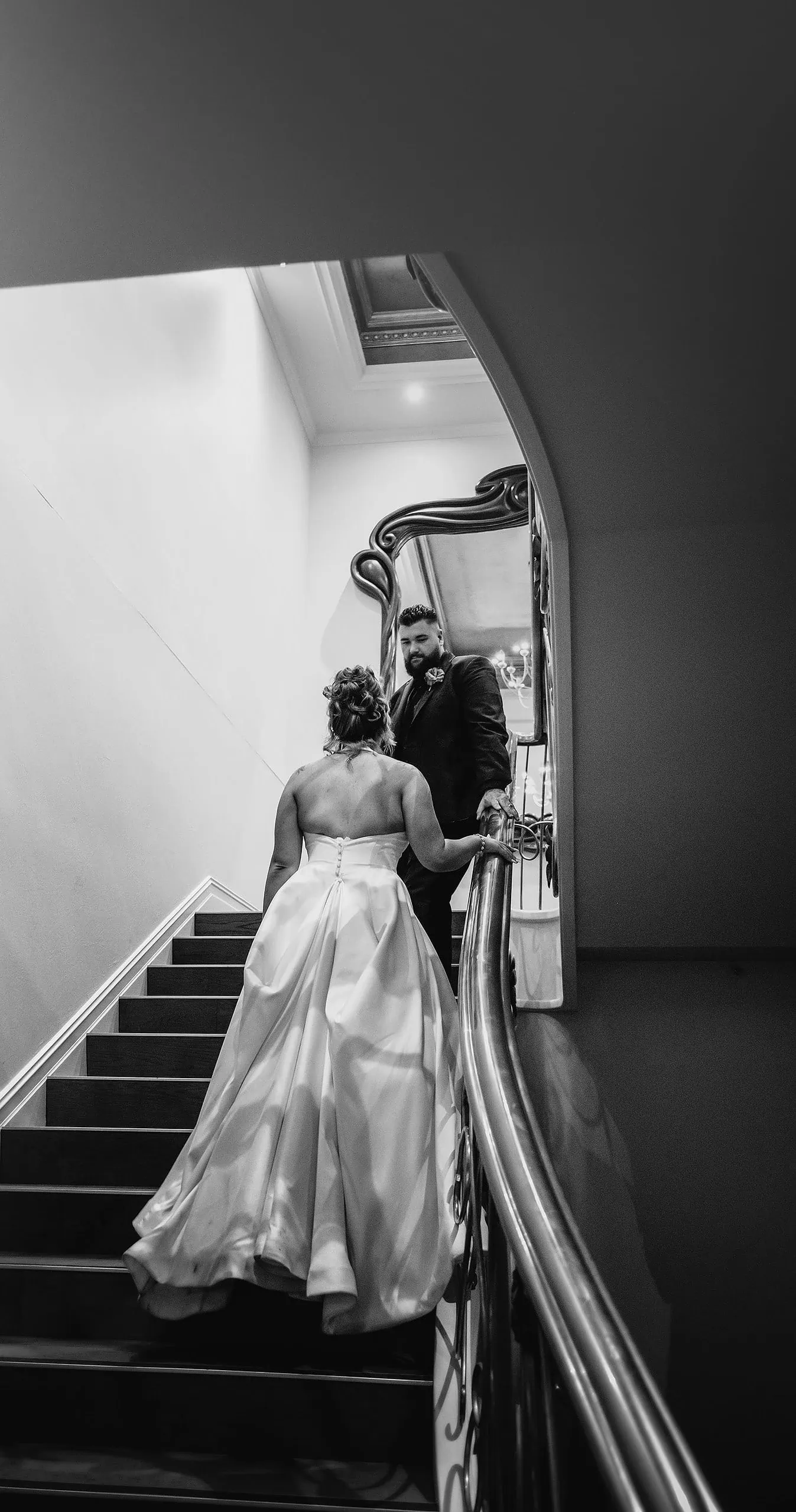 botanic gardens, araucaria avenue wedding - jade & hazim 75 Bride in white gown ascending elegant staircase with groom in black and white photograph.