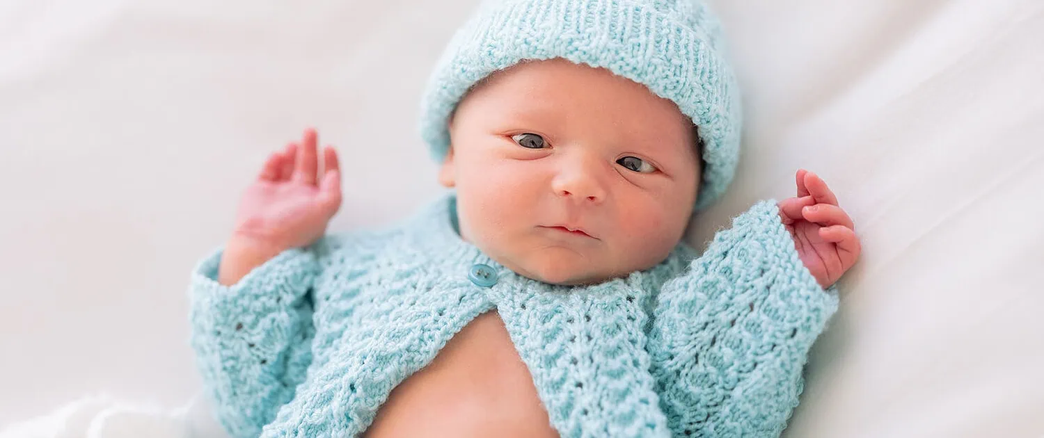 Newborn baby in blue knitwear lying peacefully on a white blanket.