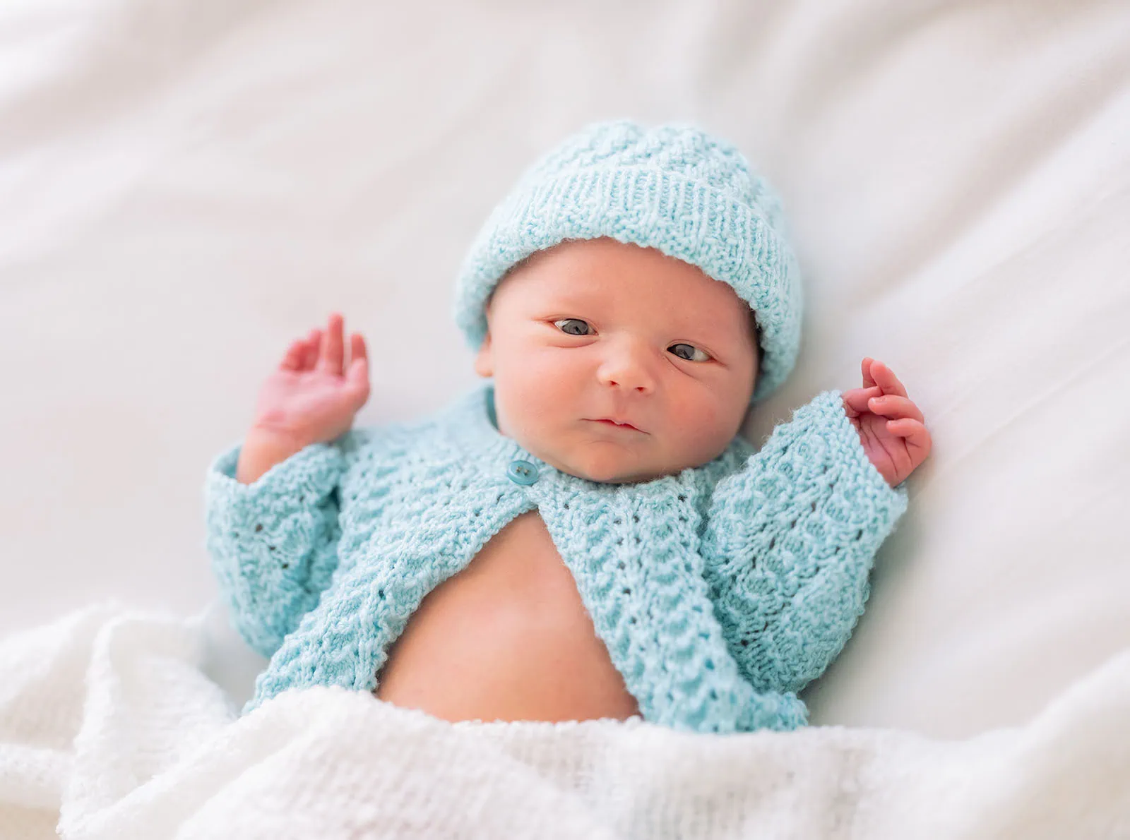 baby spencer's newborn shoot 76 Newborn baby in blue knitwear lying peacefully on a white blanket.