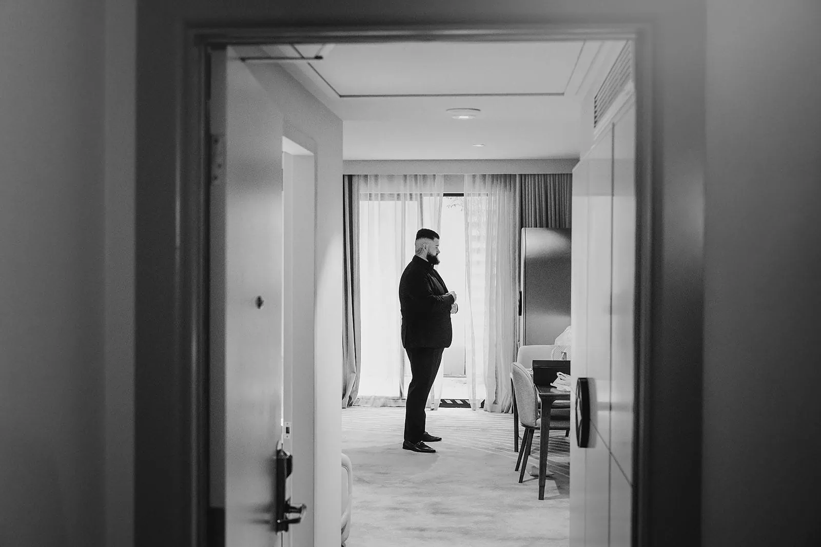botanic gardens, araucaria avenue wedding - jade & hazim 7 Man in suit using smartphone in a modern, minimalist hotel room in black and white.