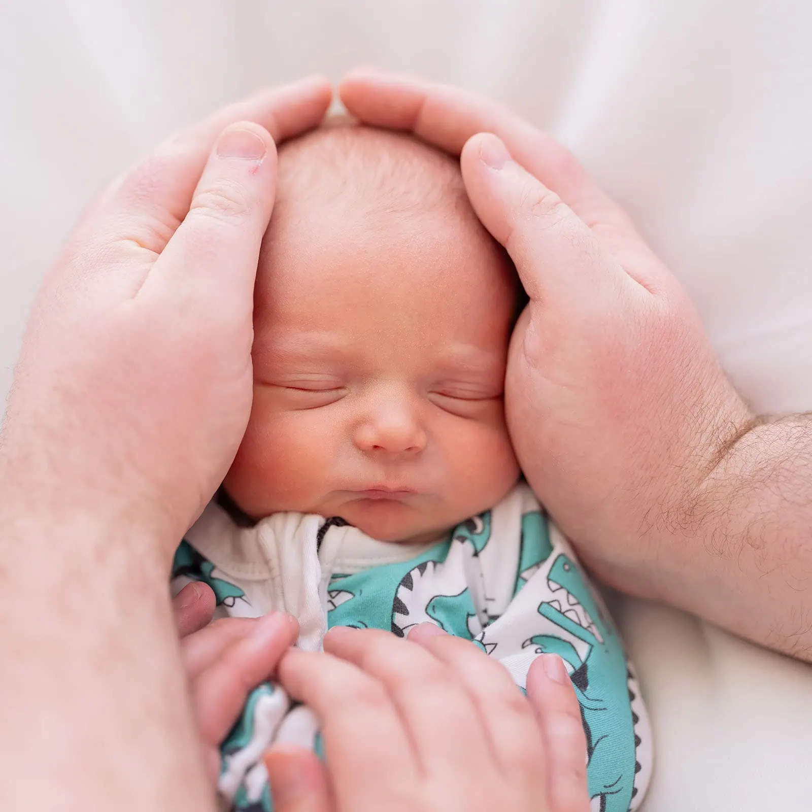 baby spencer's newborn shoot 66 Peaceful newborn baby cradled in protective adult hands, dressed in a colorful garment.