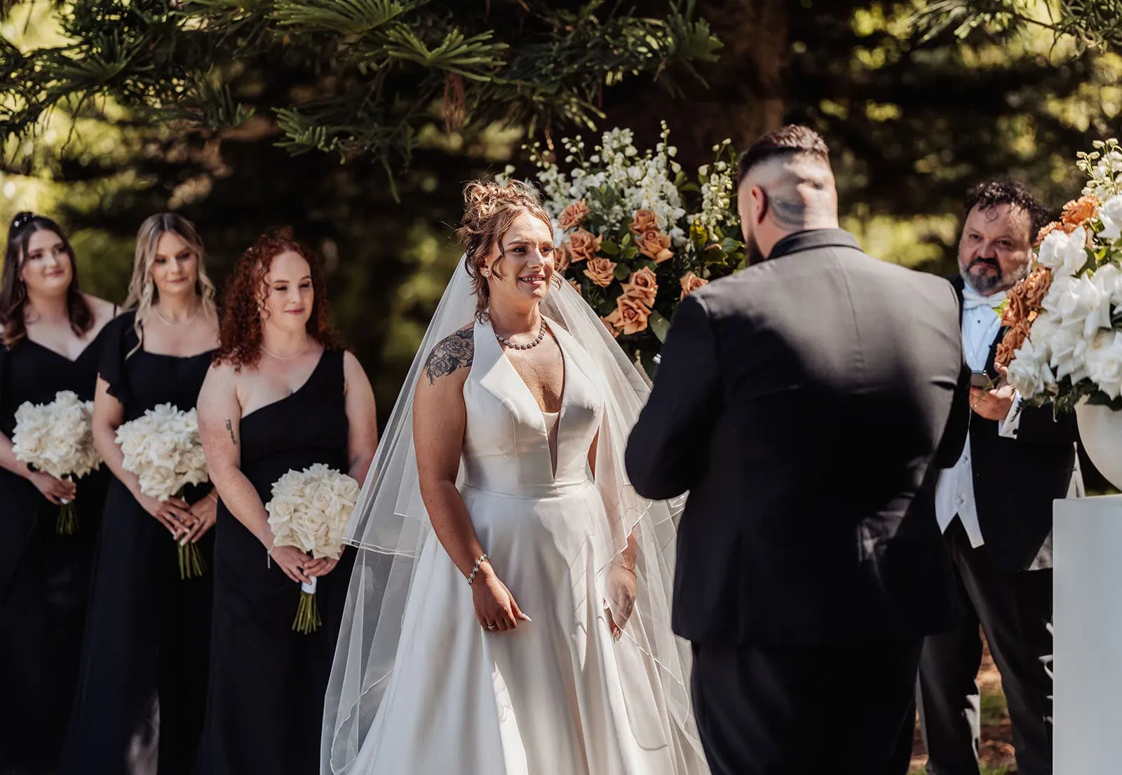 botanic gardens, araucaria avenue wedding - jade & hazim 37 Bride and groom at sunny outdoor wedding ceremony with bridesmaids and floral decor.