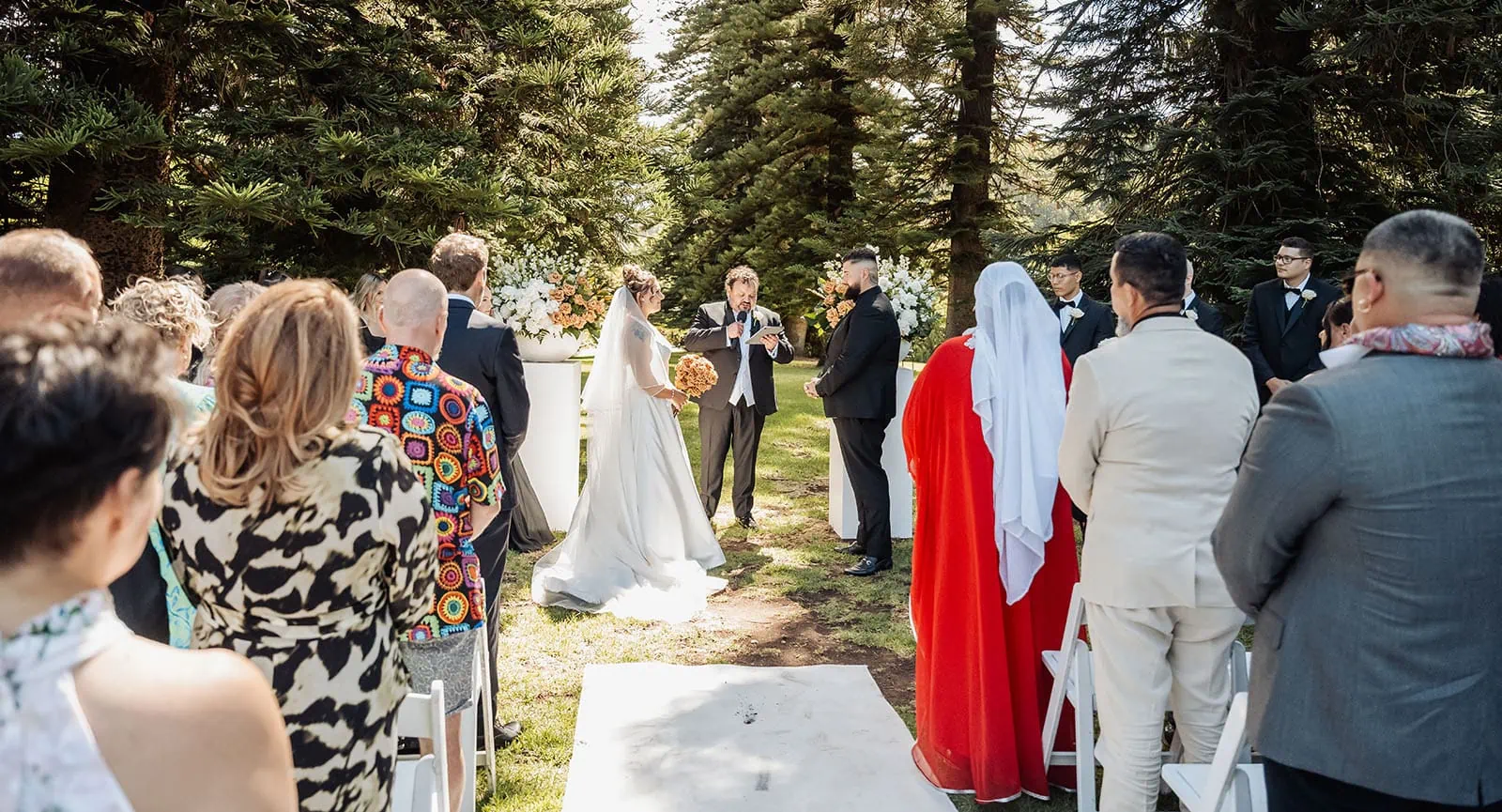 botanic gardens, araucaria avenue wedding - jade & hazim 33 Bride and groom exchanging vows in sunlit, lush green, outdoor wedding ceremony.