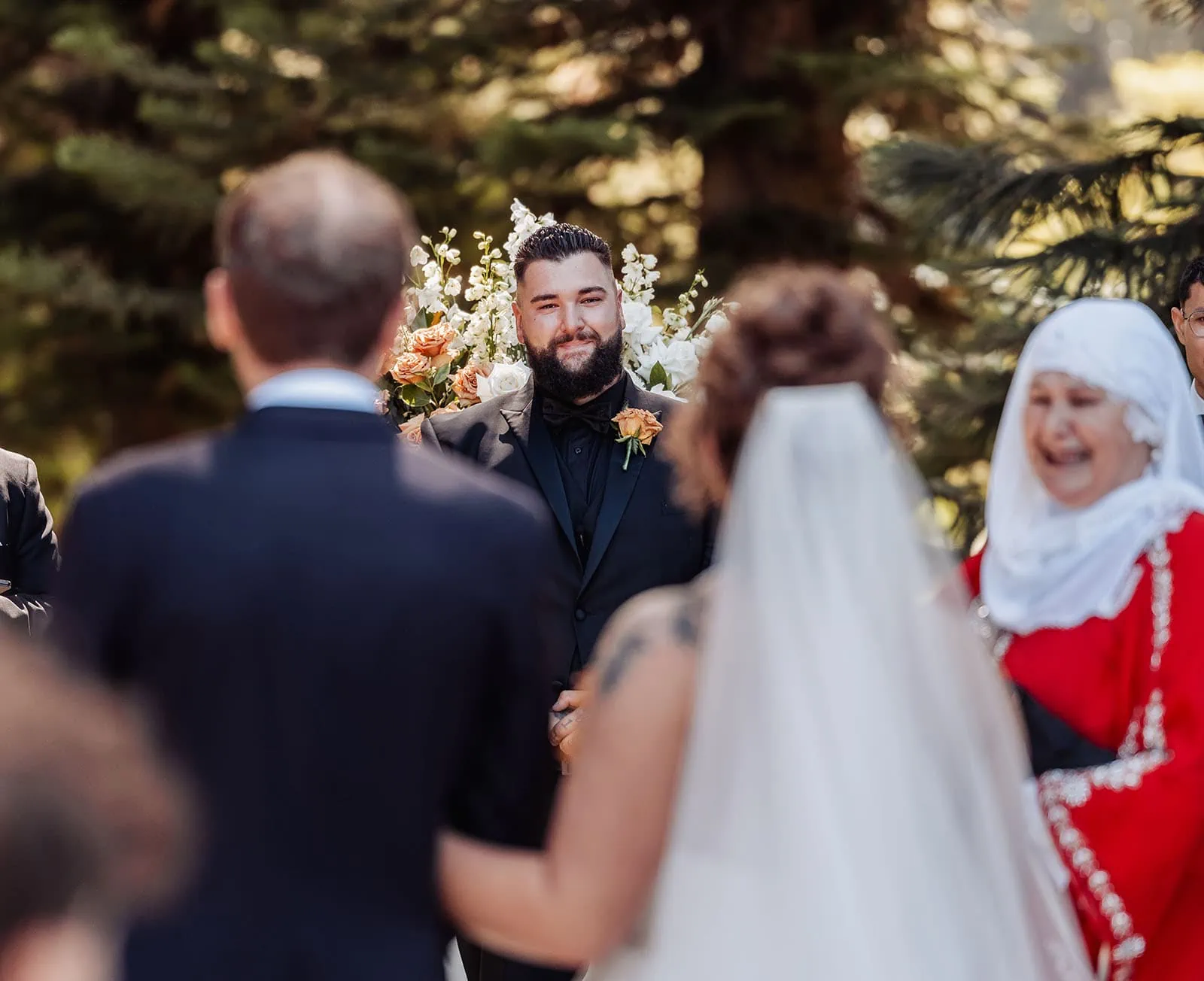 botanic gardens, araucaria avenue wedding - jade & hazim 32 Groom smiling in anticipation at outdoor wedding ceremony with bride and officiant.
