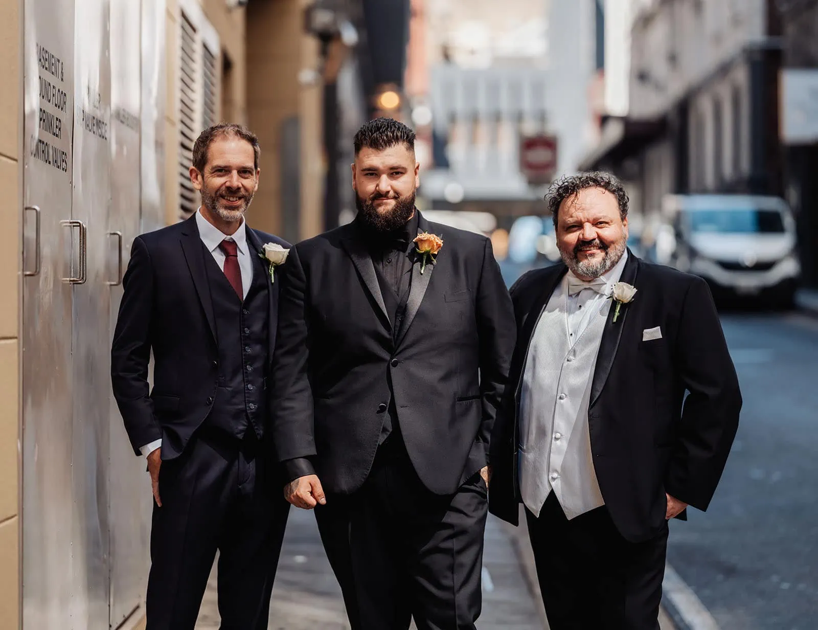 botanic gardens, araucaria avenue wedding - jade & hazim 11 Three formally dressed men sharing a moment in an urban alleyway during daytime.
