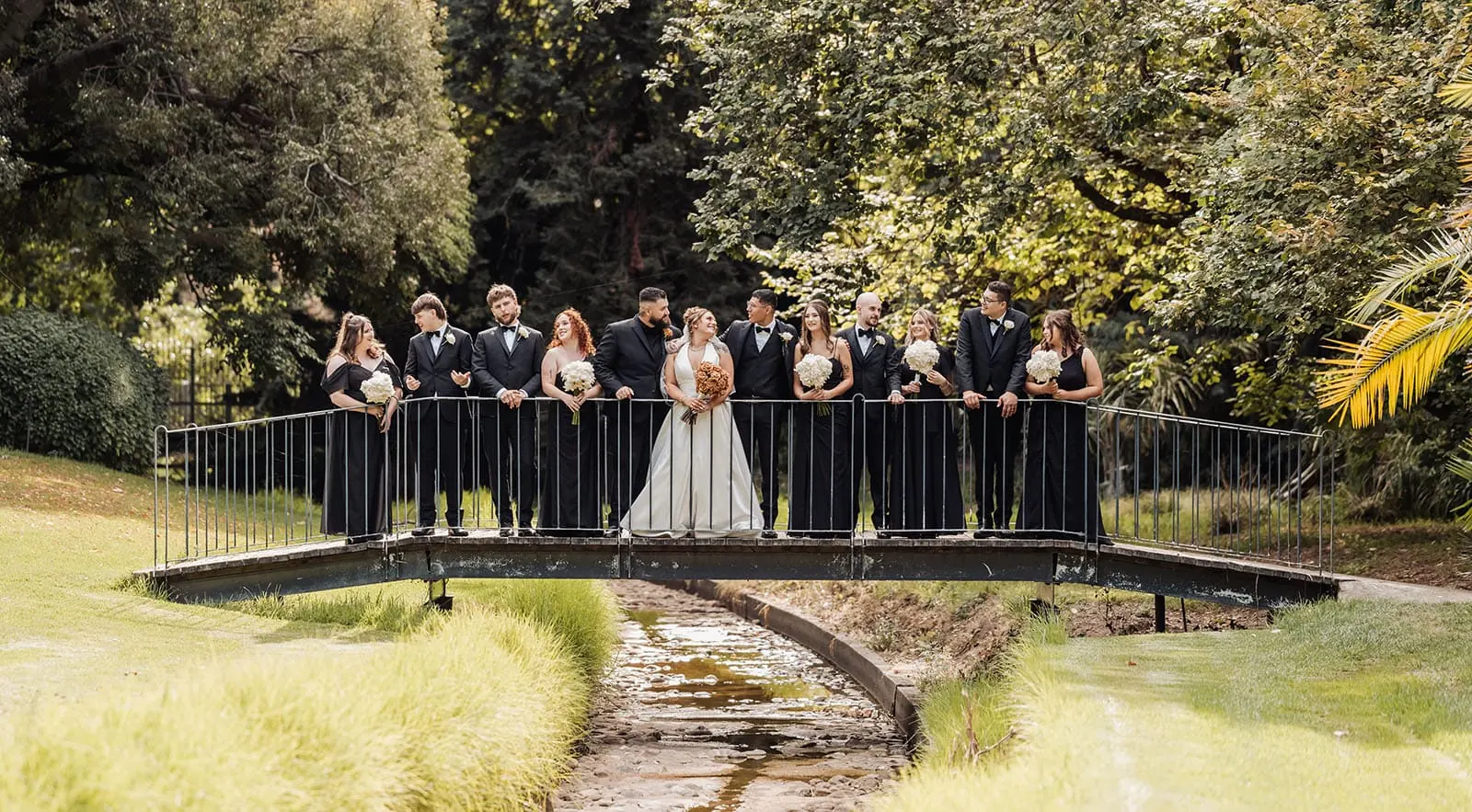 botanic gardens, araucaria avenue wedding - jade & hazim 47 Bride and groom with wedding party on garden bridge in summer celebration.