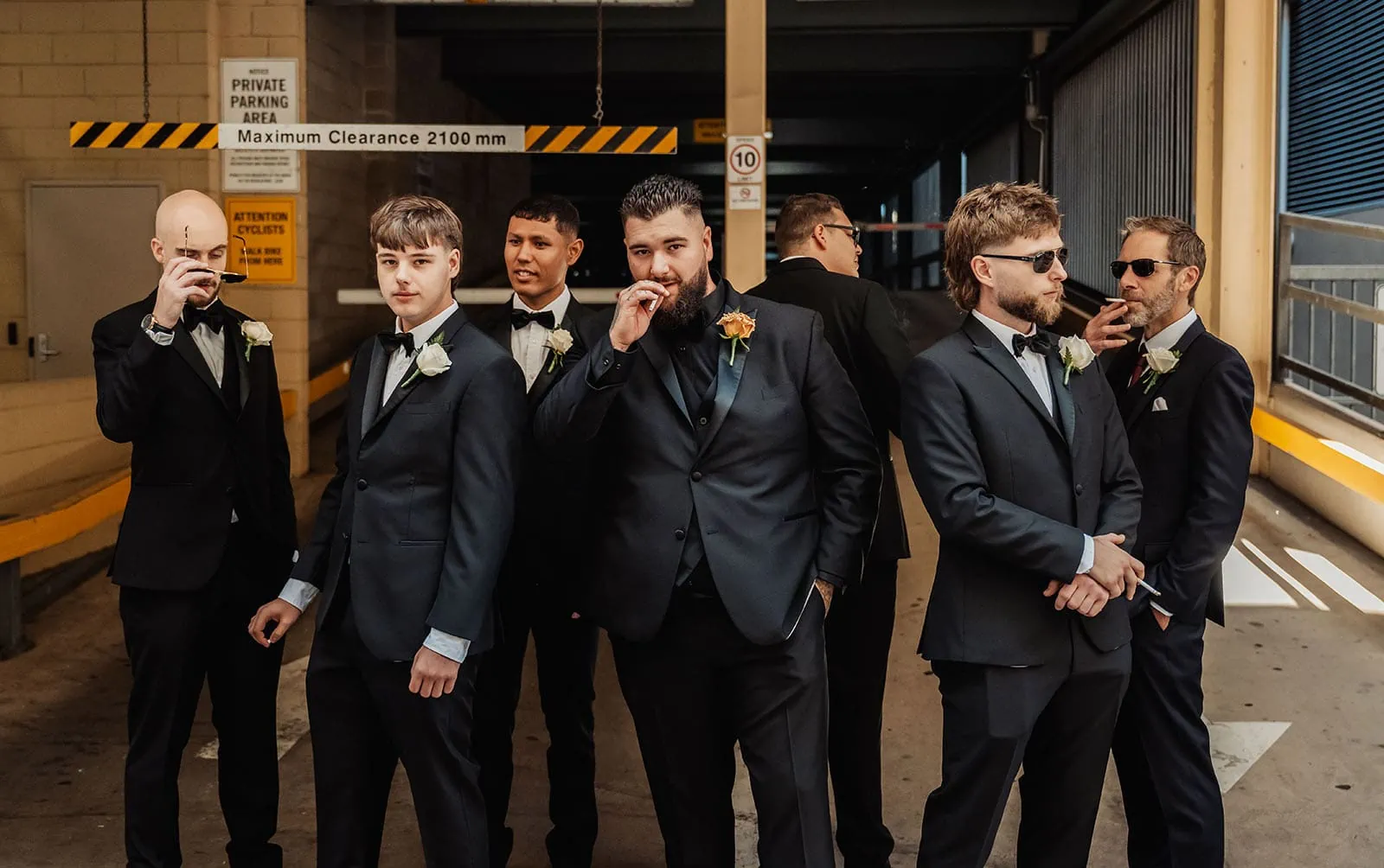 botanic gardens, araucaria avenue wedding - jade & hazim 9 Groomsmen in suits sharing a casual moment in an urban parking garage.