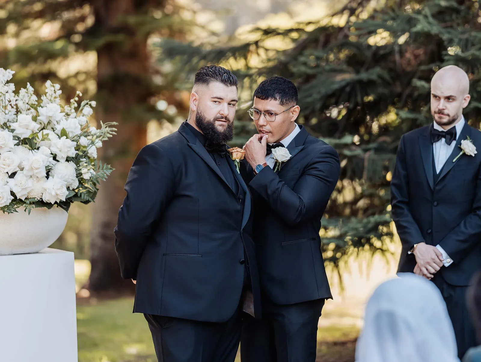 botanic gardens, araucaria avenue wedding - jade & hazim 30 Two groomsmen in formal attire at an outdoor wedding ceremony.