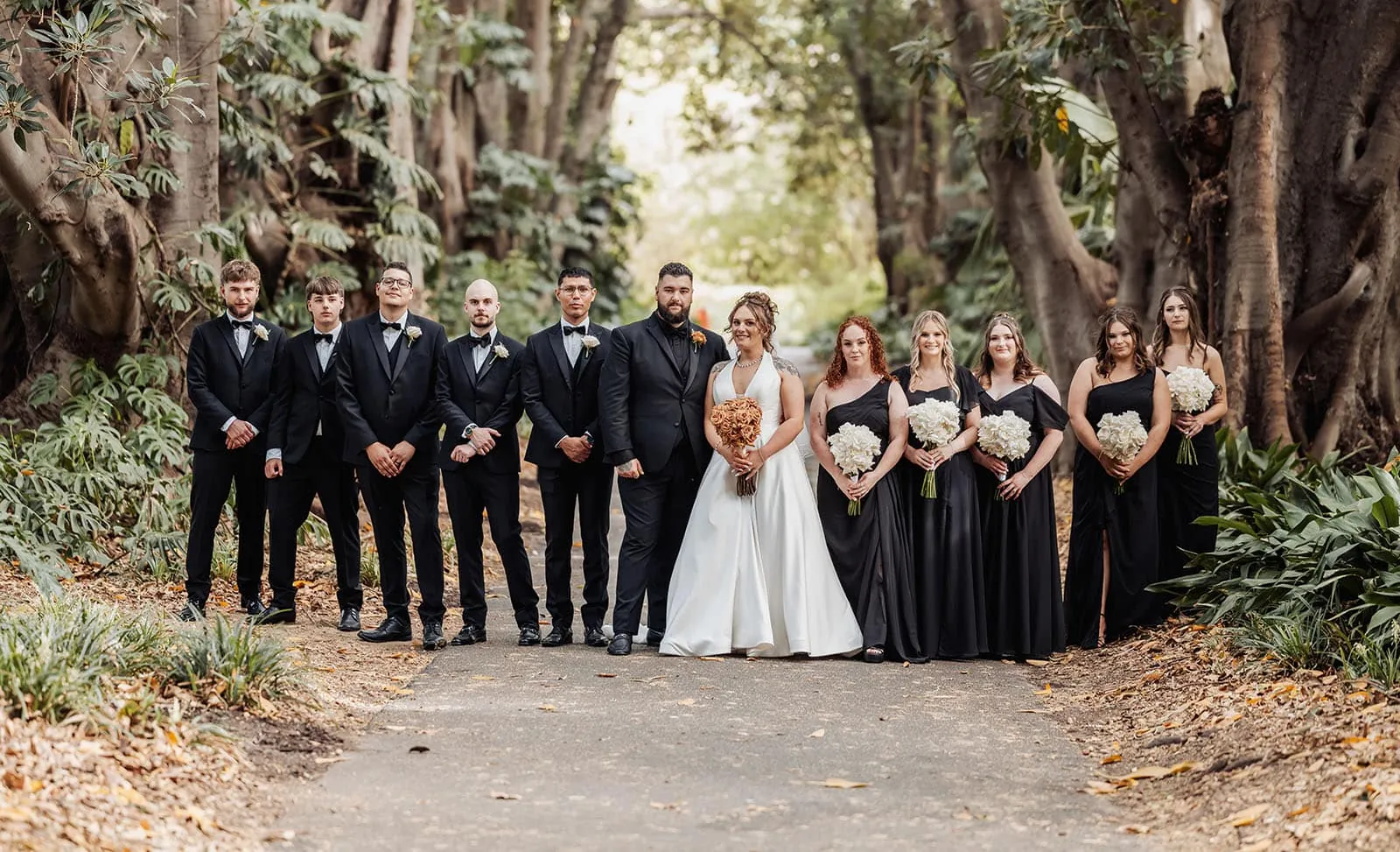 botanic gardens, araucaria avenue wedding - jade & hazim 50 Newlywed couple with wedding party in fall outdoor setting.