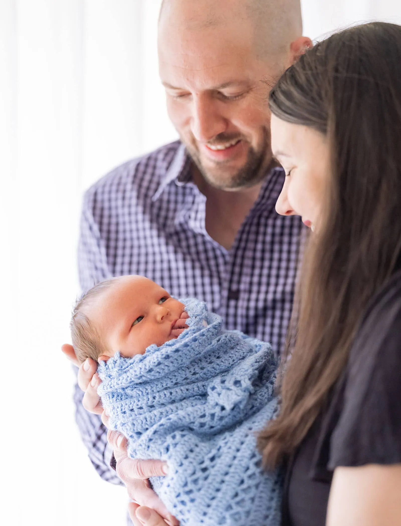 baby joshua's newborn photo shoot 37 Family holding newborn baby wrapped in blue blanket, expressing love and joy.