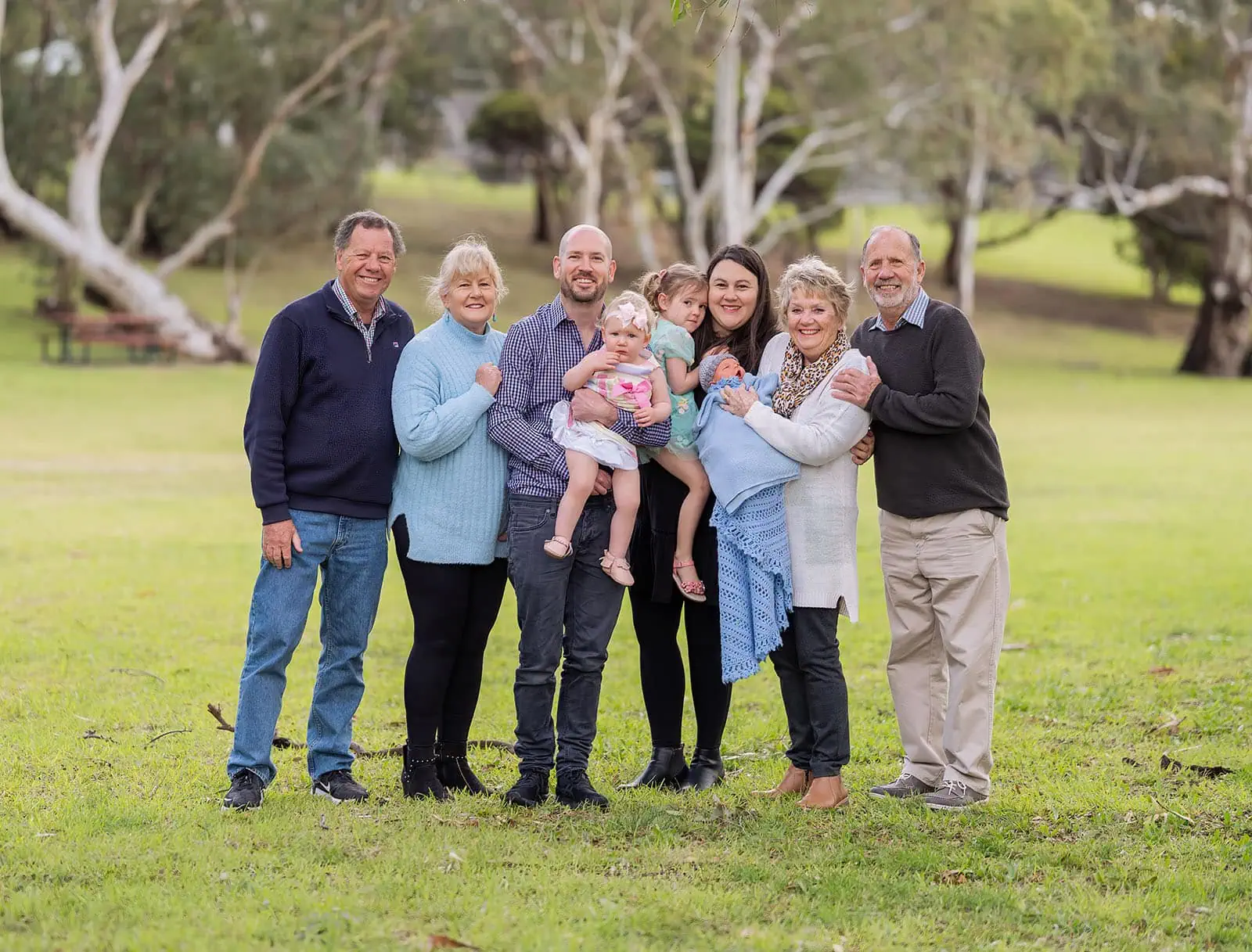 baby joshua's newborn photo shoot 31 Multi-generational family smiling together in park.