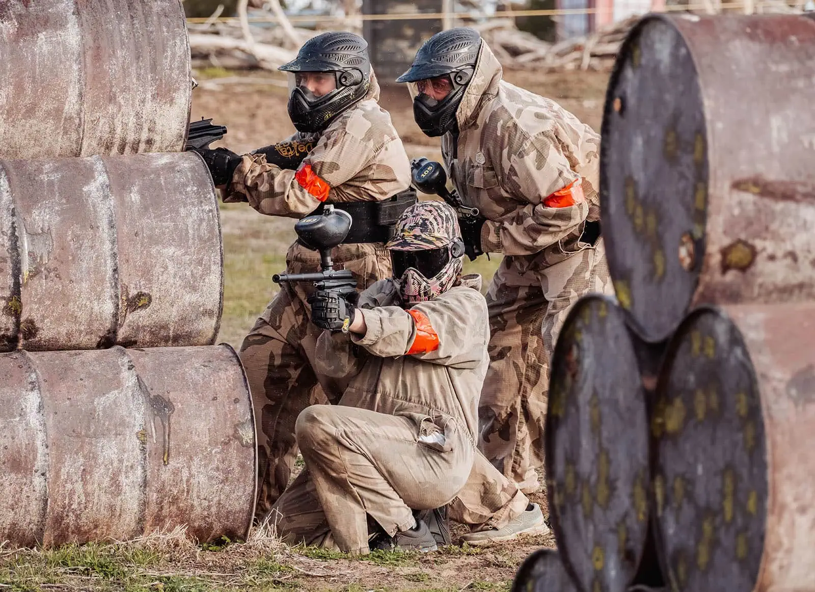 monarto delta force bucks vs hens paintball party 28 Paintball players in action, using barrels for cover on an outdoor field.