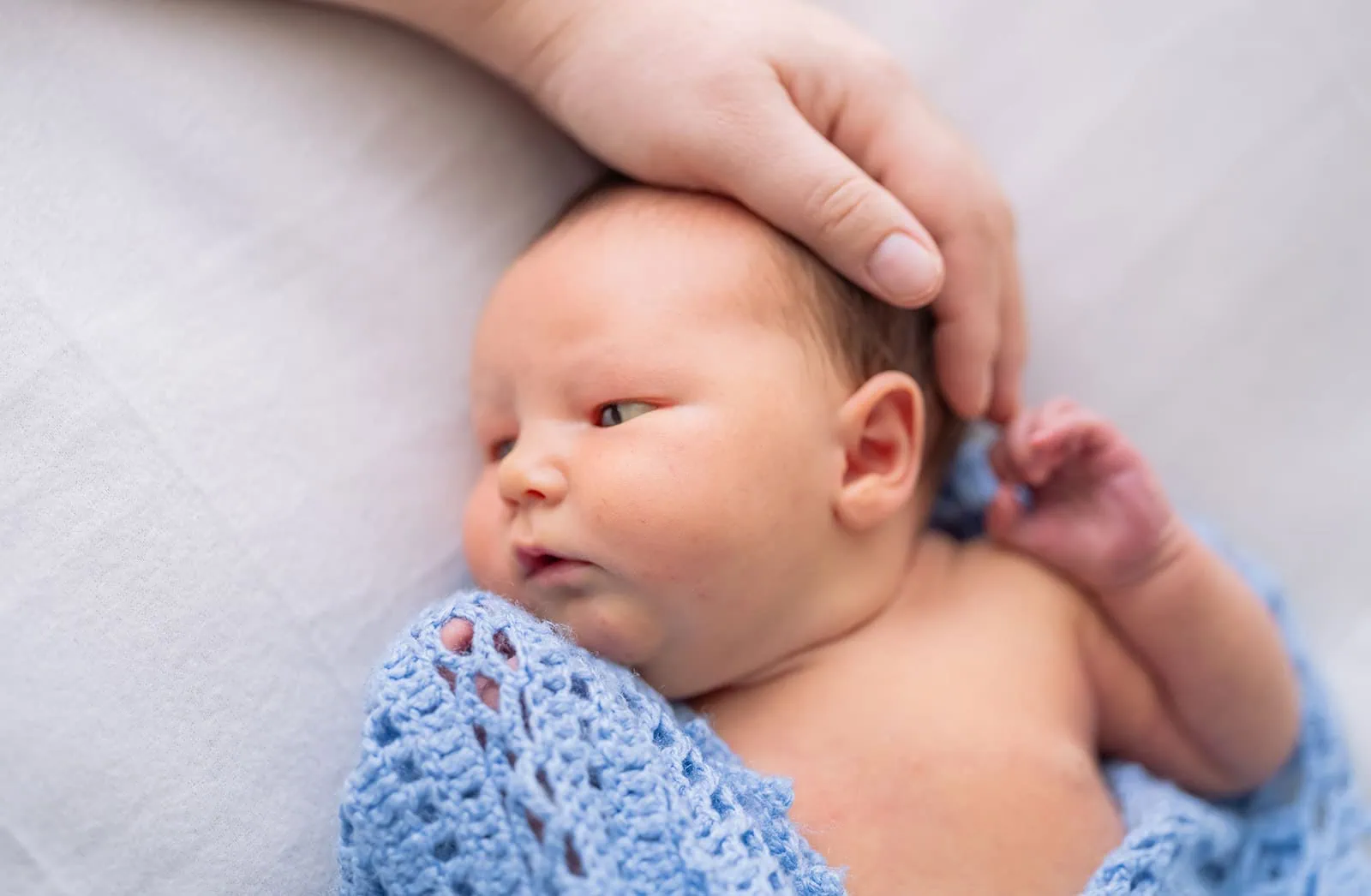 baby joshua's newborn photo shoot 40 Newborn baby wrapped in a blue knitted blanket, cradled by a parents hand.