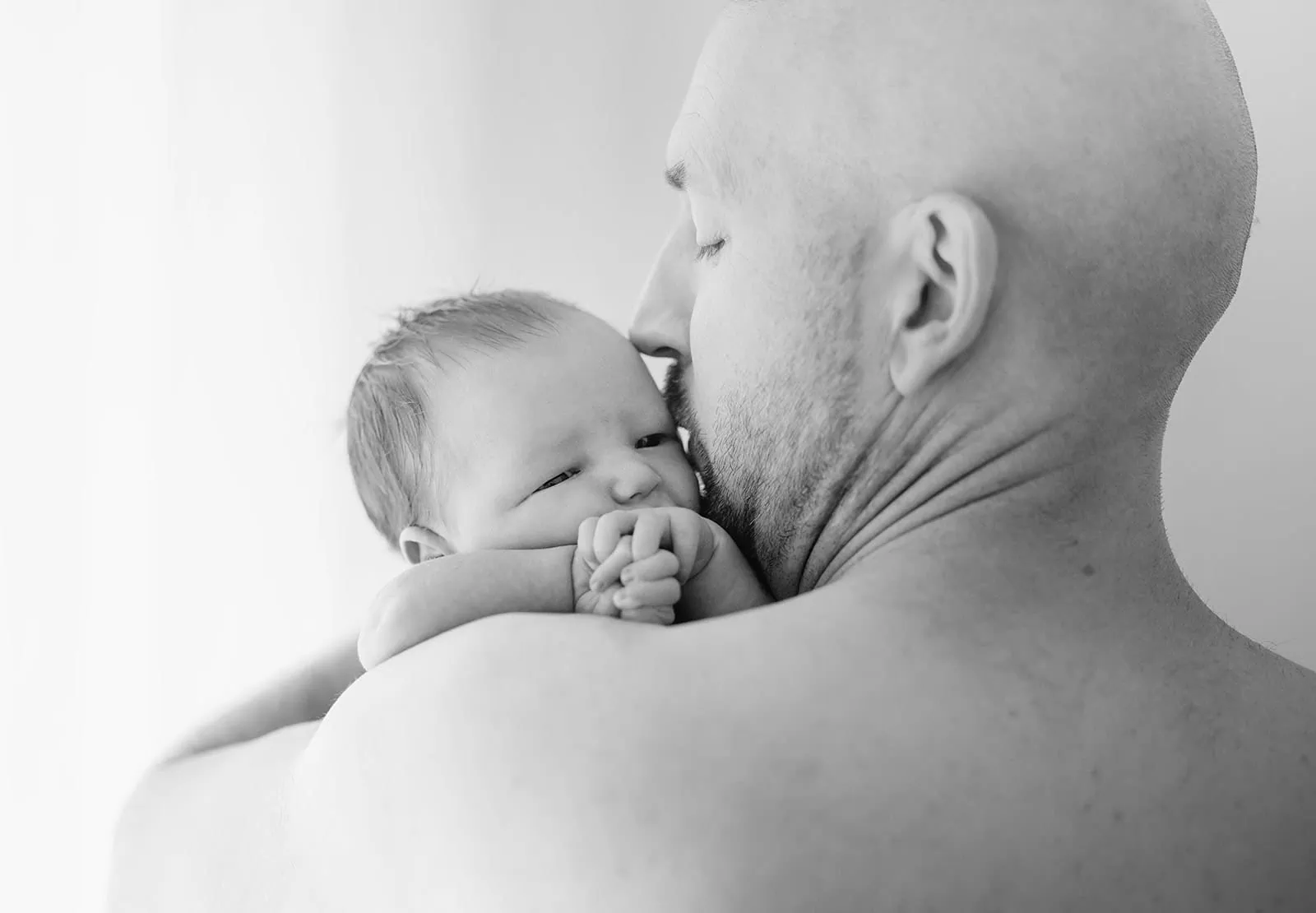baby joshua's newborn photo shoot 38 Father kissing newborn baby on shoulder, capturing love and bond.