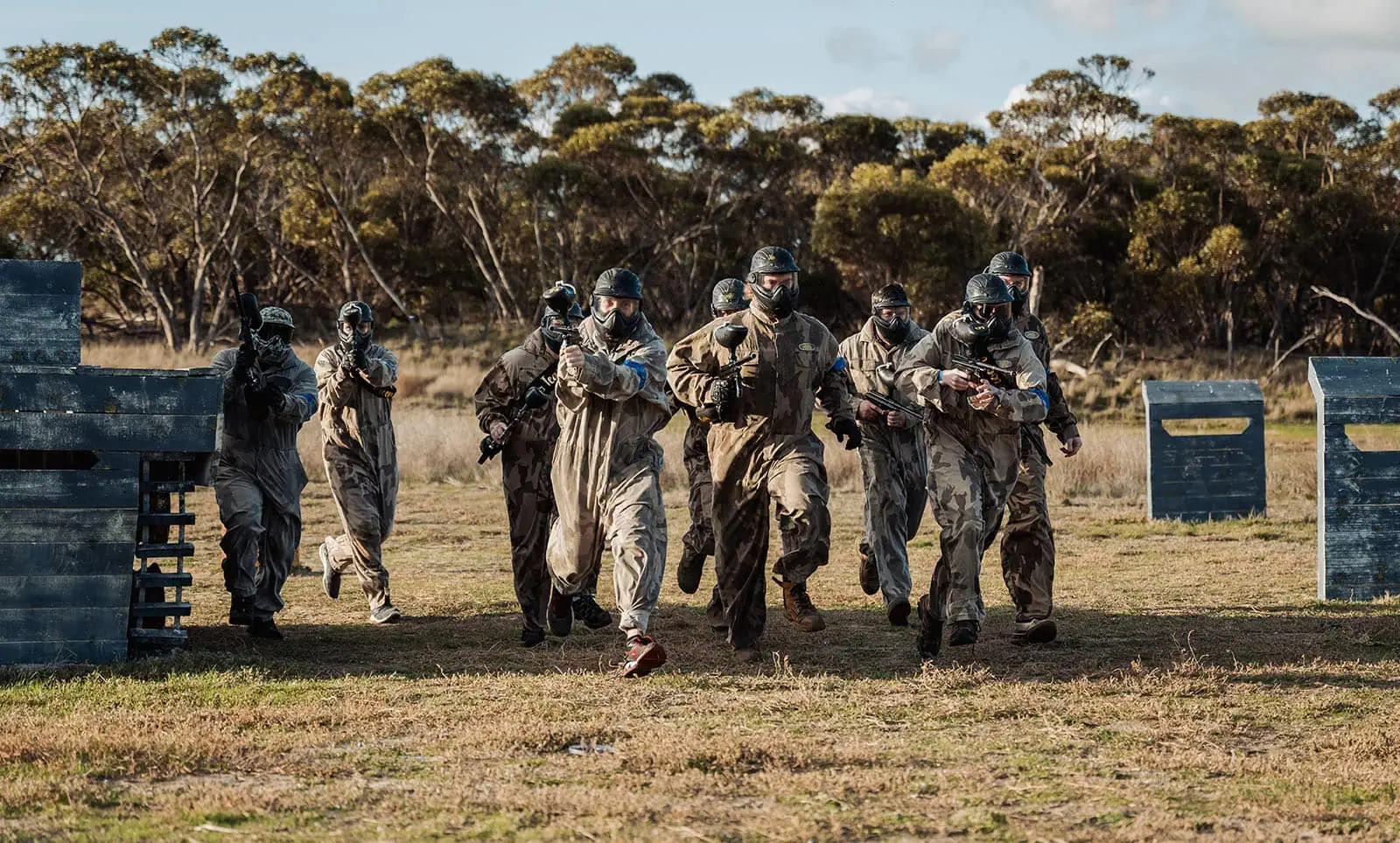 monarto delta force bucks vs hens paintball party 33 Paintball players in action on a forest field, running and strategizing with paintball guns.