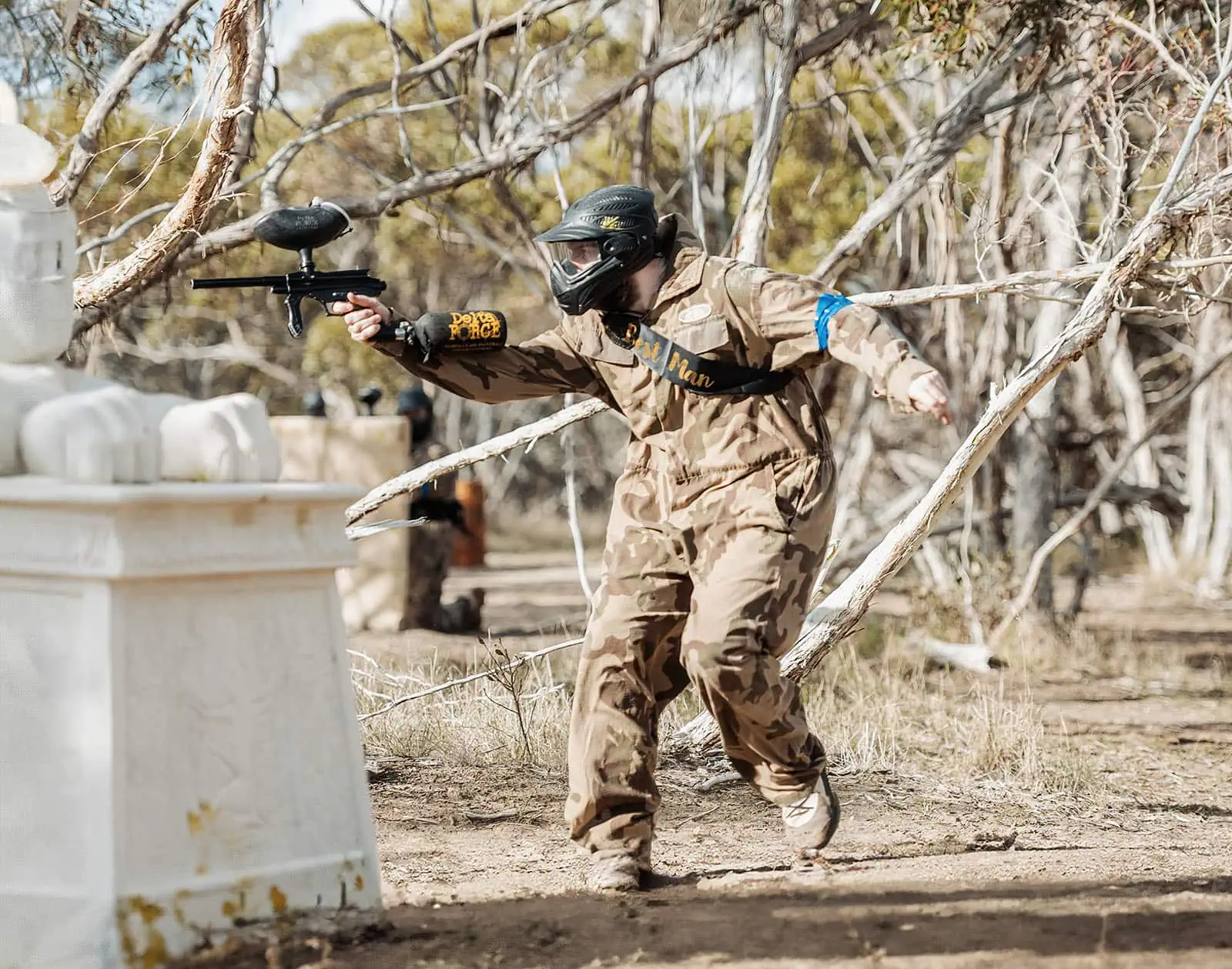 monarto delta force bucks vs hens paintball party 18 Paintball player in camouflage gear aiming gun in forested field with lion statue.