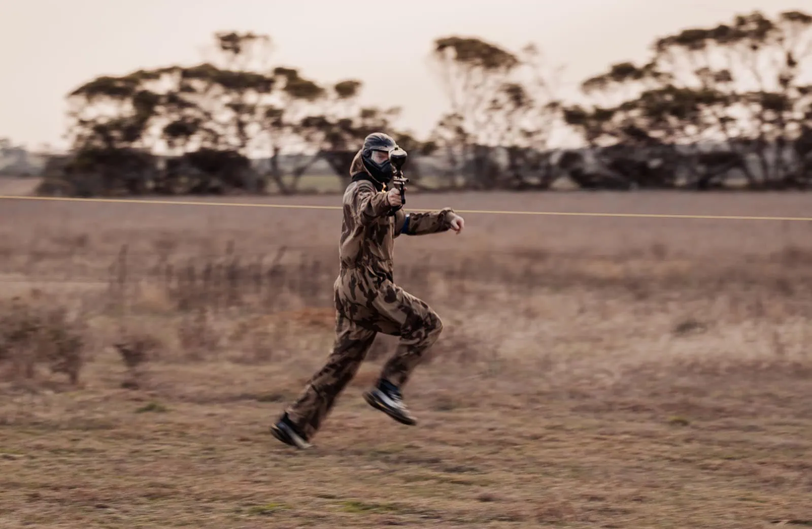 monarto delta force bucks vs hens paintball party 37 Paintball player running across field in camouflage gear and mask, holding paintball gun.