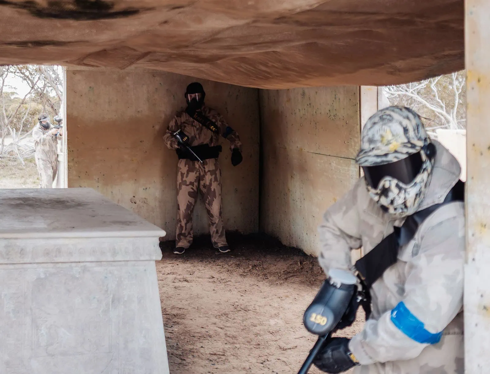 monarto delta force bucks vs hens paintball party 16 Paintball players in action inside concrete structure, wearing camouflage gear and protective masks.