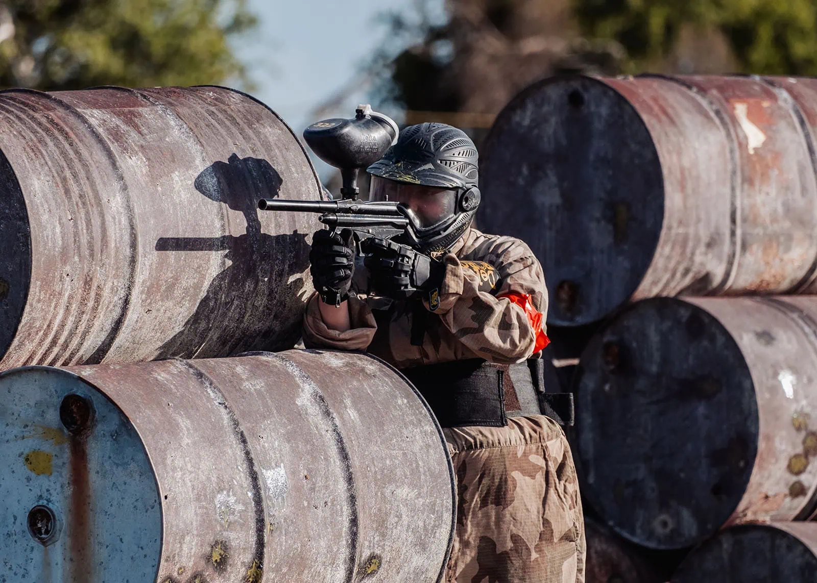 monarto delta force bucks vs hens paintball party 25 Paintball player aiming marker behind barrels in outdoor game.