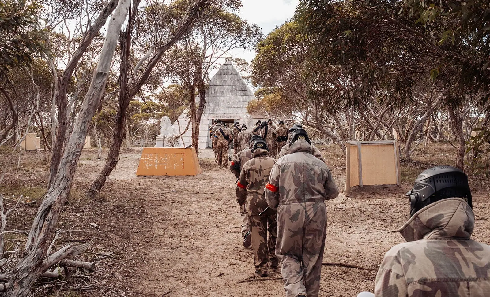 monarto delta force bucks vs hens paintball party 12 Paintball players in camo gear approach a stone pyramid in a wooded area.