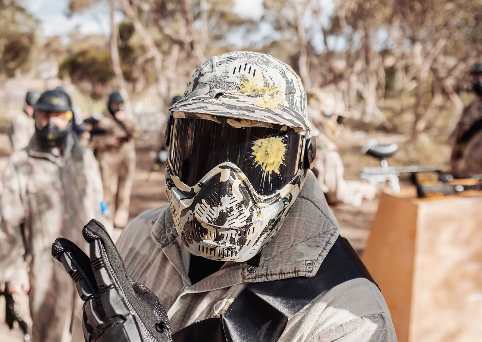 monarto delta force bucks vs hens paintball party 17 Paintball players in camouflage gear with yellow paint splatters, signaling peace in forest setting.