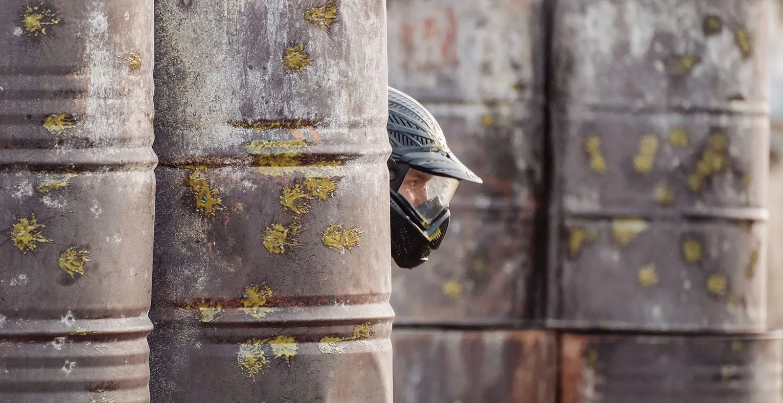 monarto delta force bucks vs hens paintball party 32 Paintball player hiding behind paint-splattered barrels in an industrial setting.