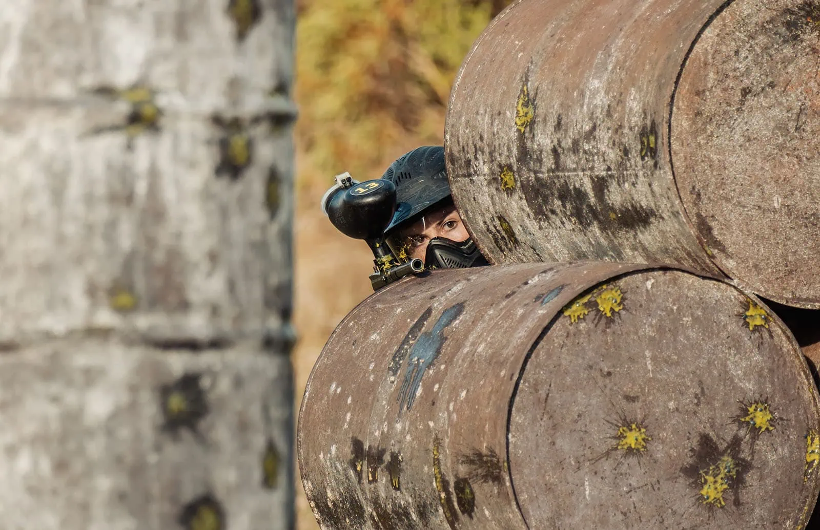 monarto delta force bucks vs hens paintball party 30 Paintball player hiding behind paint-splattered barrels, ready to shoot.